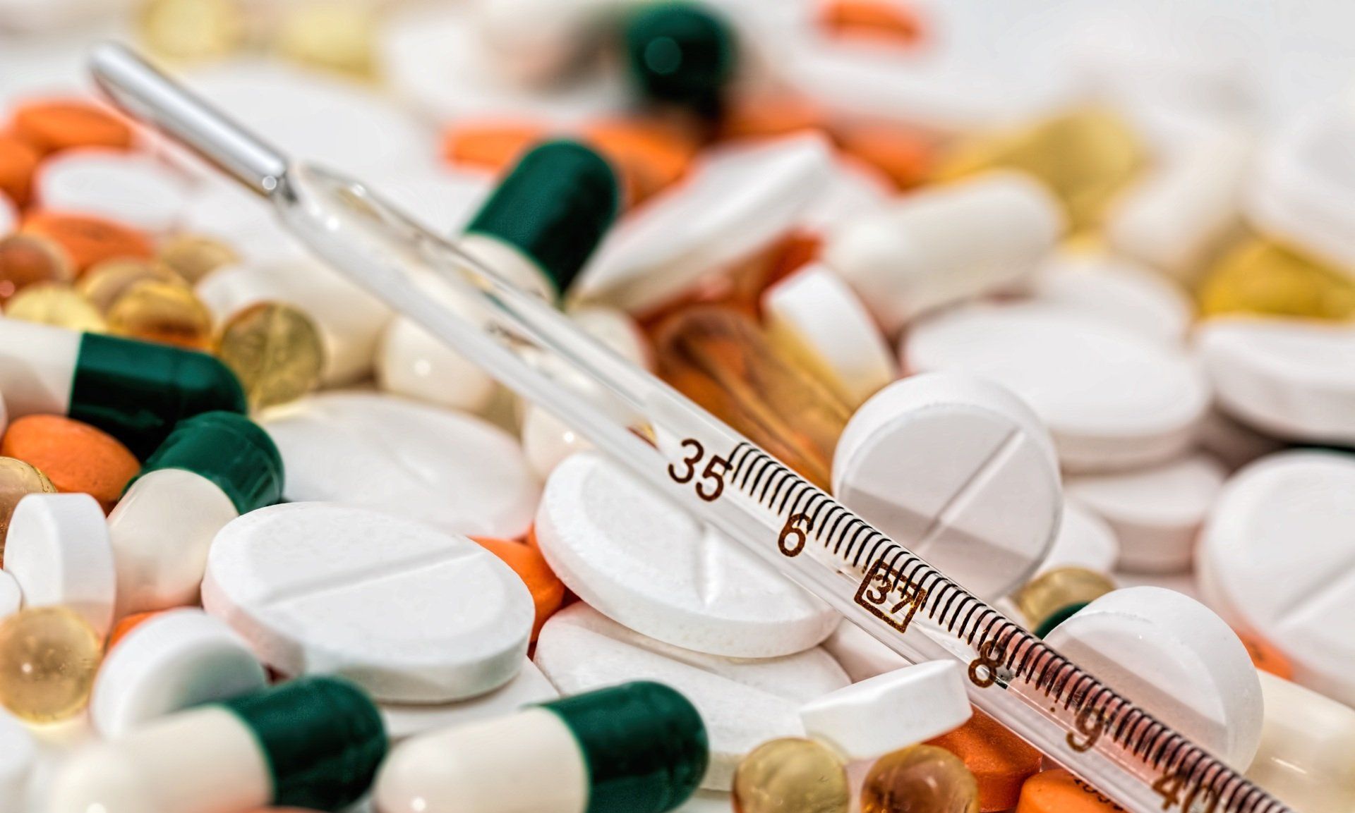 A thermometer is sitting on top of a pile of pills and capsules.
