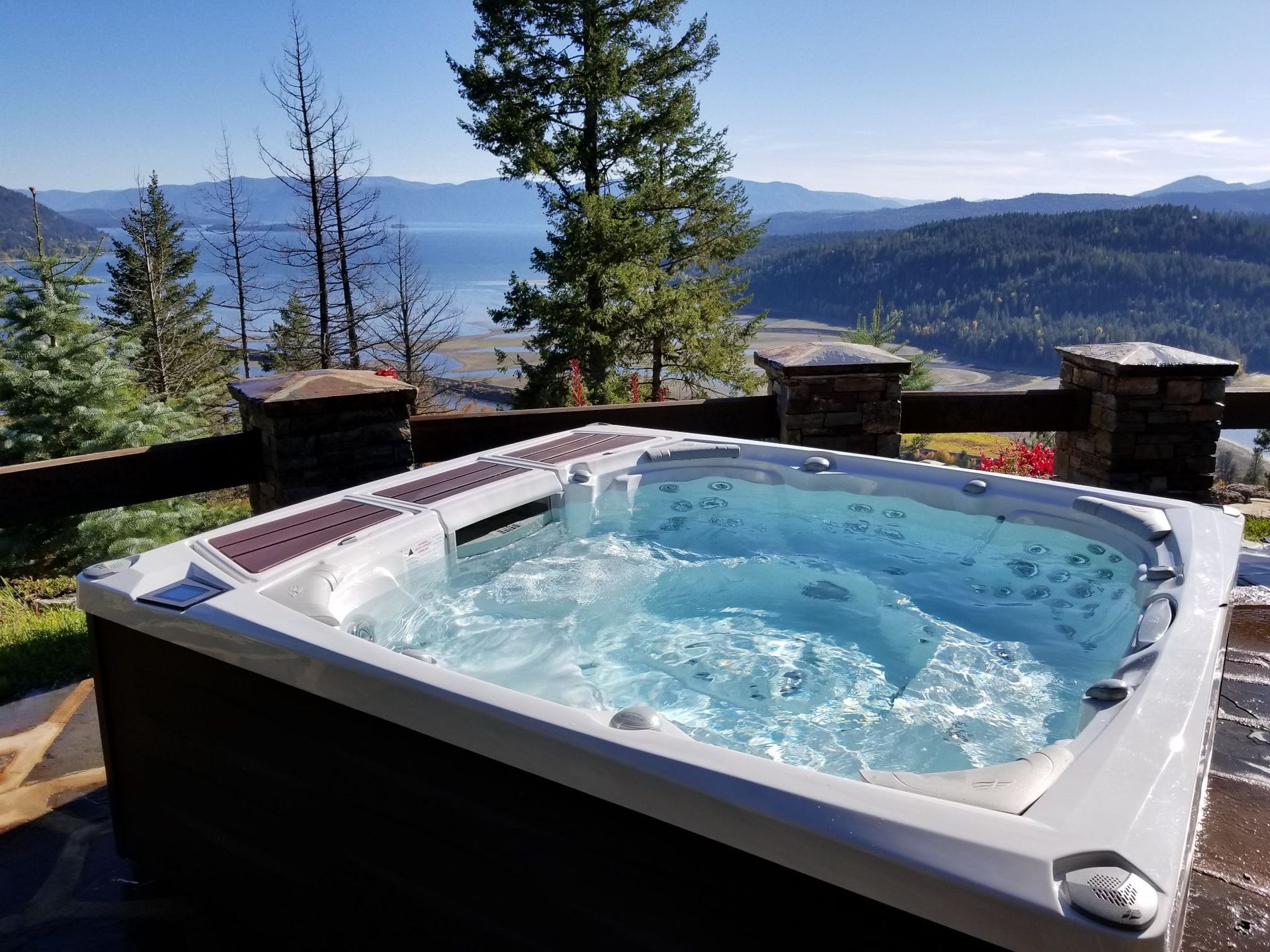 Hot tub overlooking a scenic lake and mountains on a sunny day.