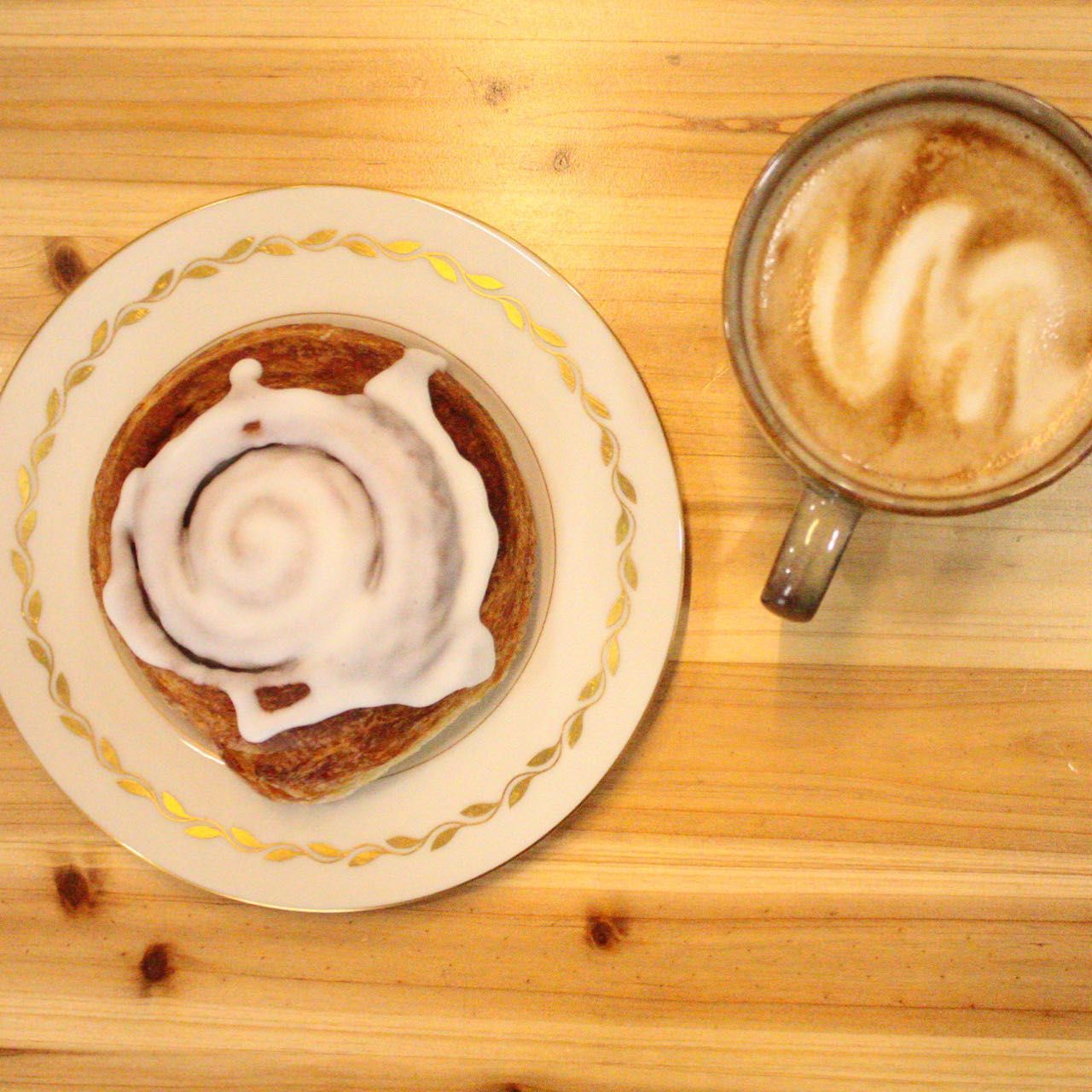 A cinnamon roll on a plate next to a cup of coffee