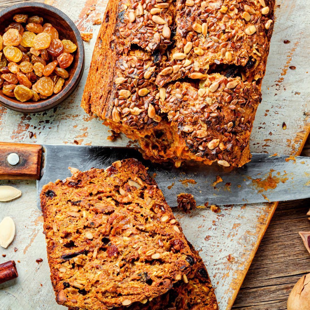 A loaf of bread is sitting on a cutting board next to a bowl of raisins.