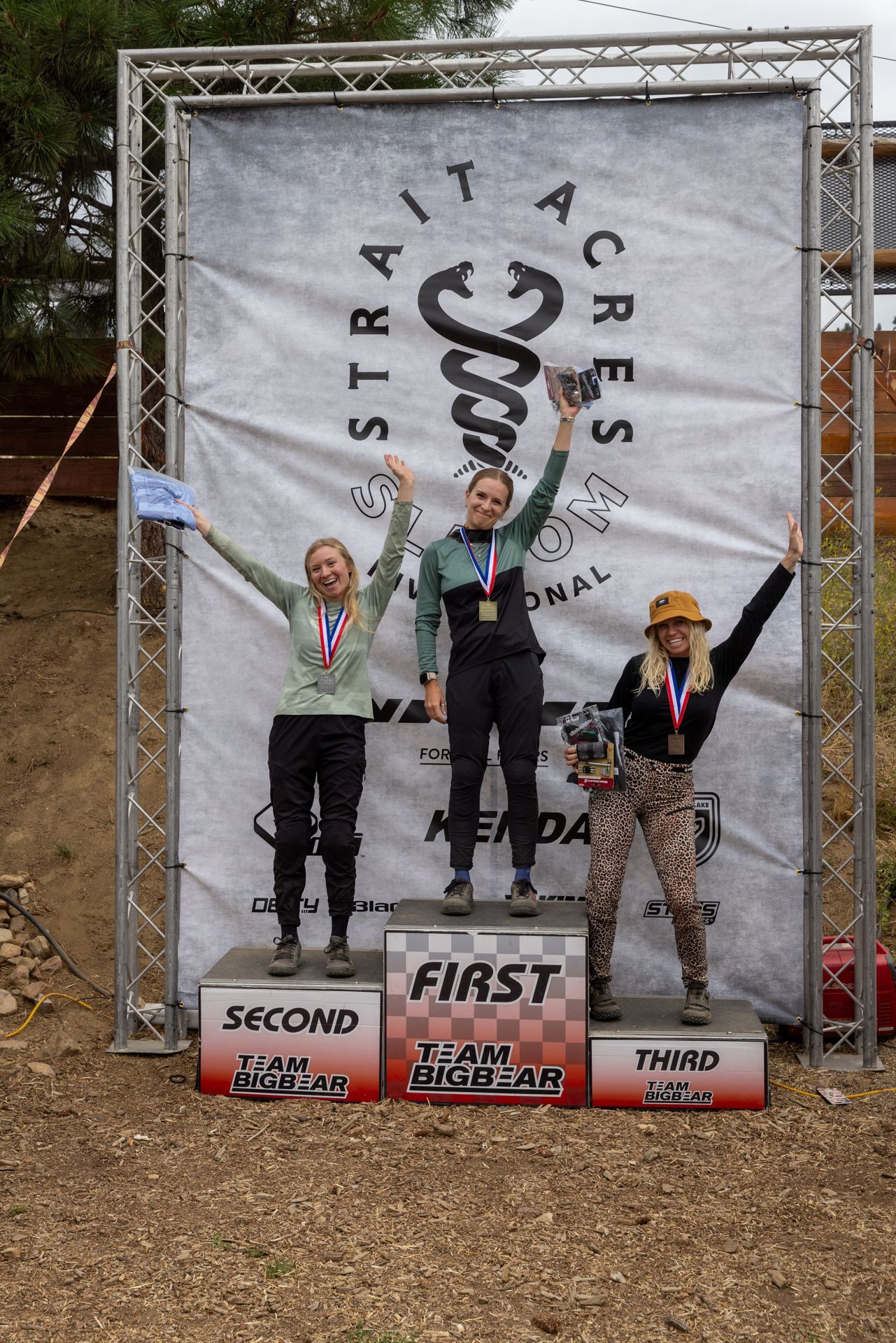 Podium with three women: First place holding a trophy, second and third place with medals