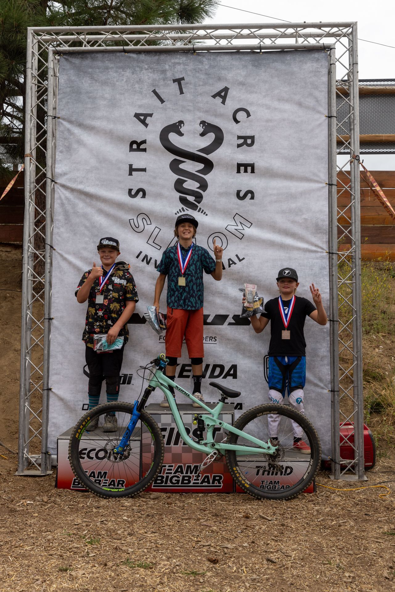 Mountain bike race podium: three young boys with medals pose in front of a banner.