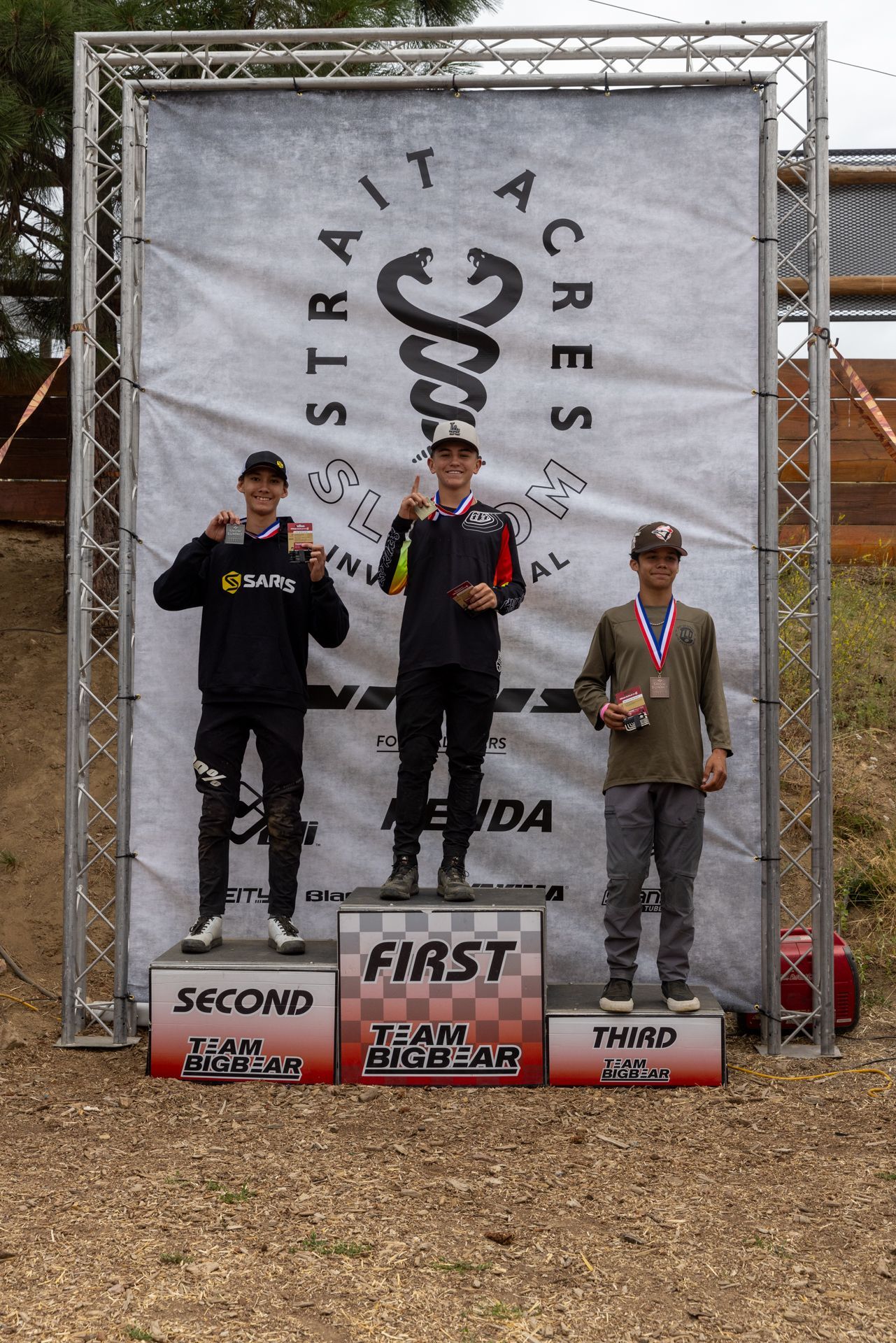 Three motocross racers stand on a podium at 