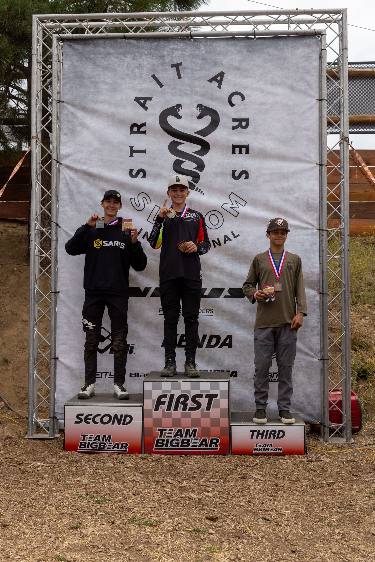 Podium at Strait Acres. Three young men stand on a podium, holding medals. The winner in the center, 