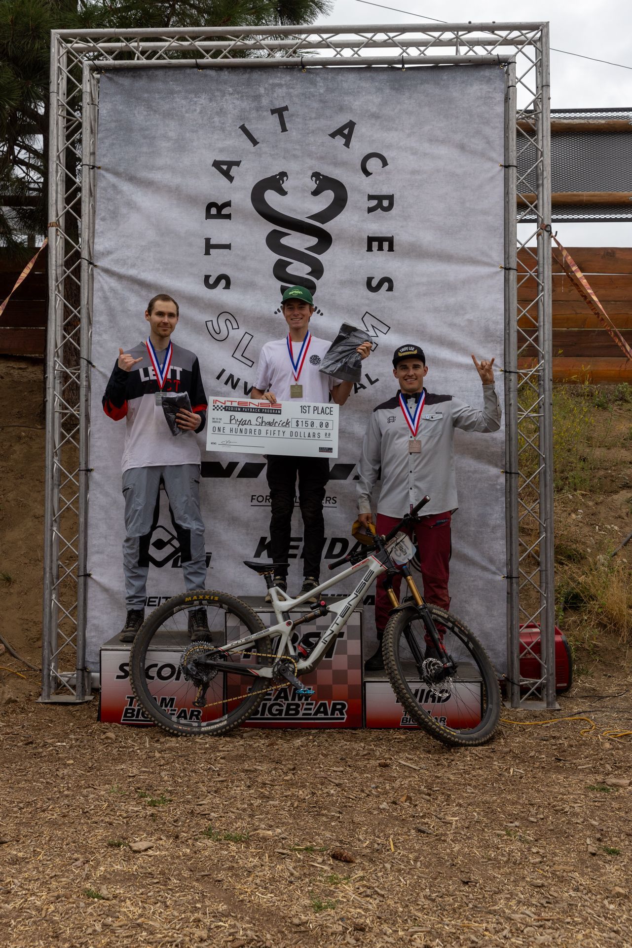 Mountain bike race podium at Strait Acres. Three men stand on the podium, holding trophies and smiling