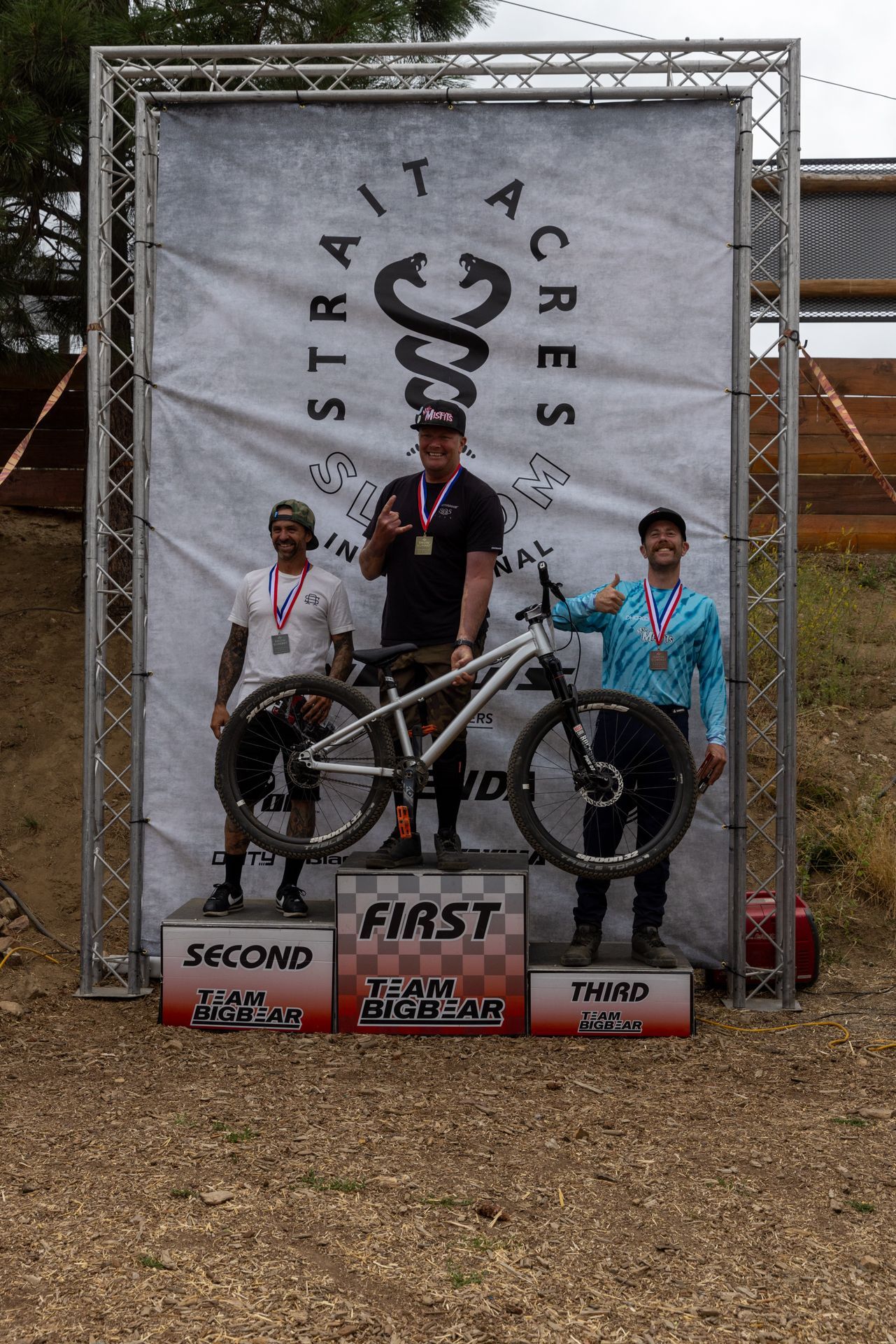 Mountain bike race podium: three men with medals stand on a platform. The first-place winner holds his bike.