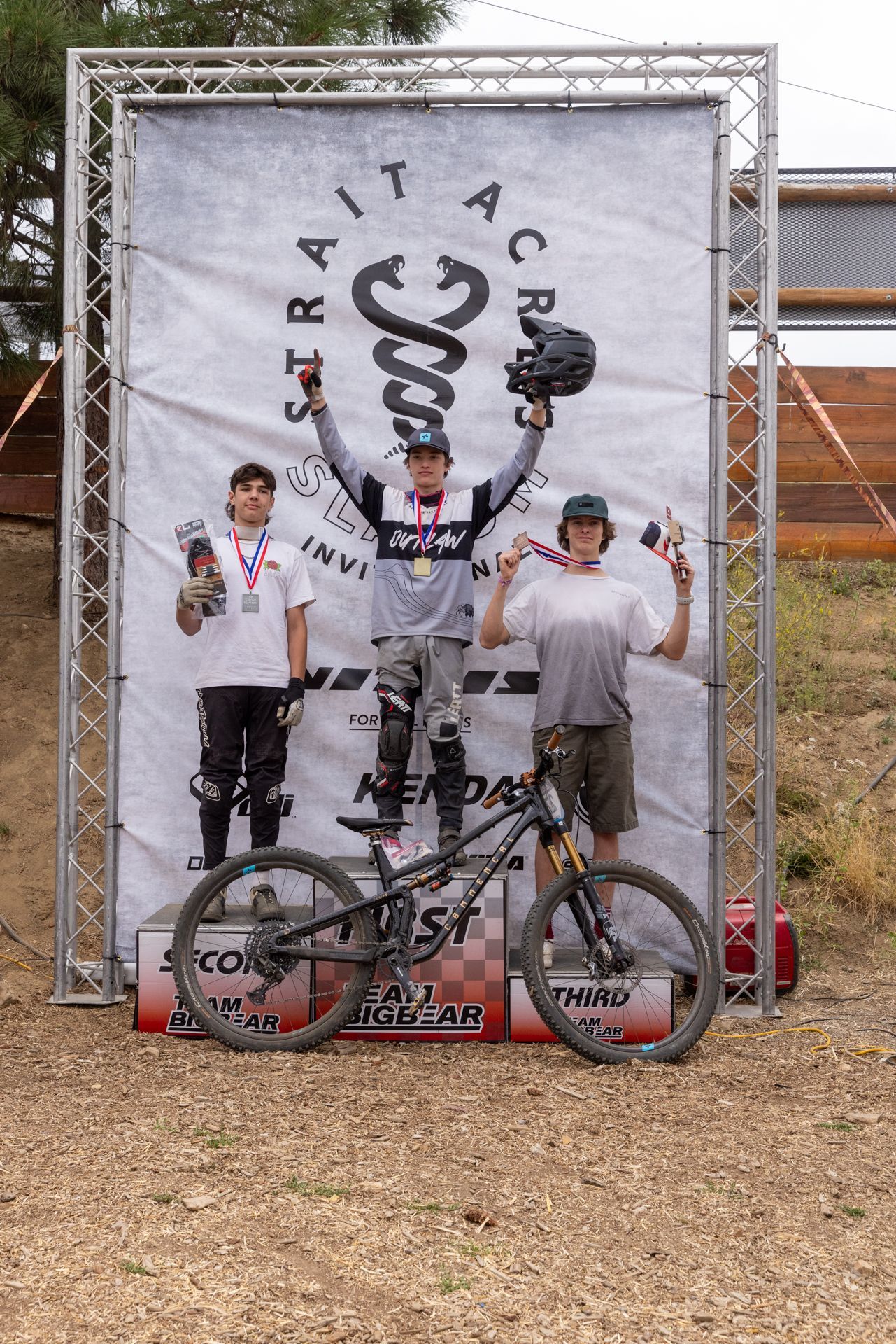 Mountain bikers on a podium holding medals and trophies at a race.