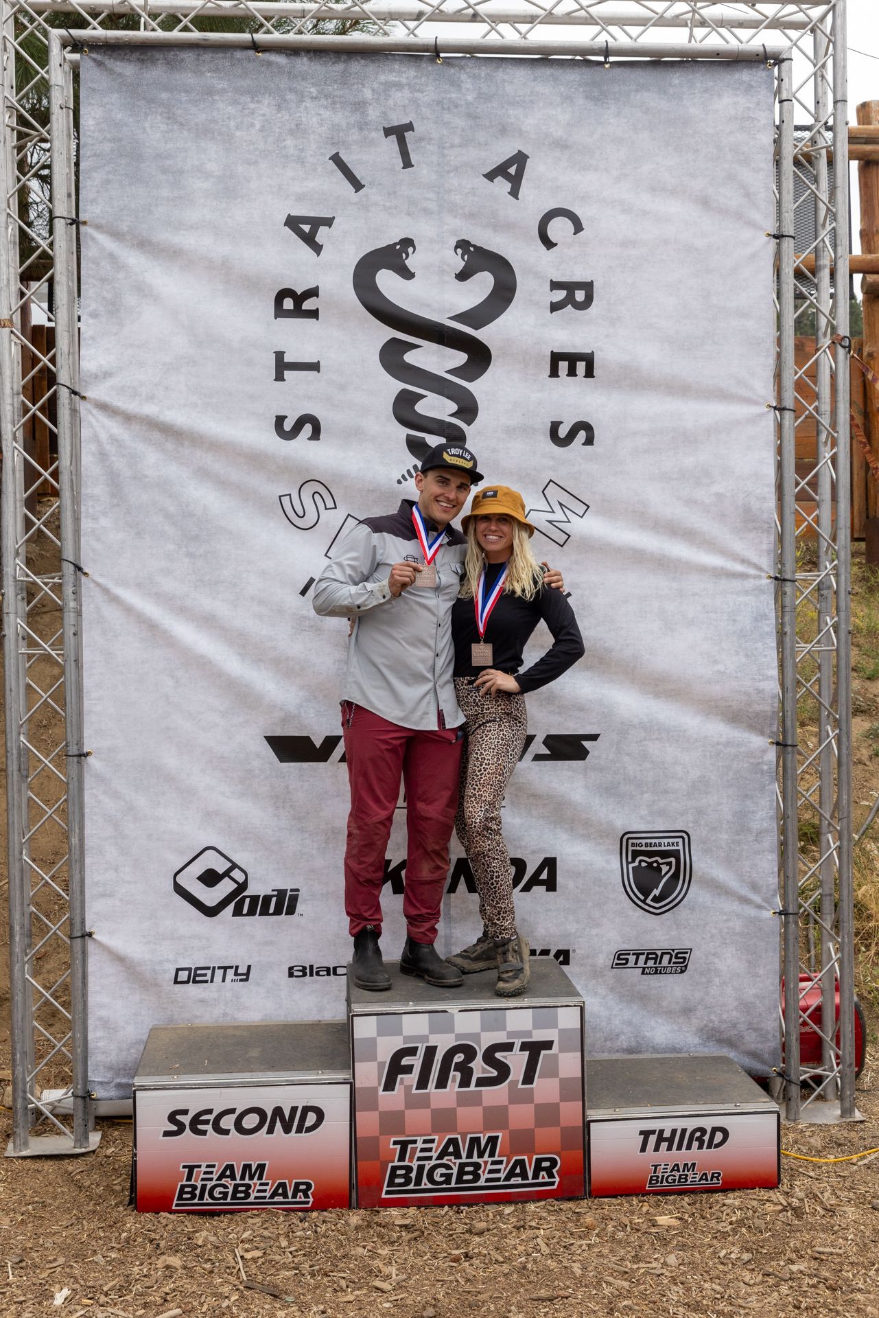 Two people stand on a podium, holding medals in front of a 