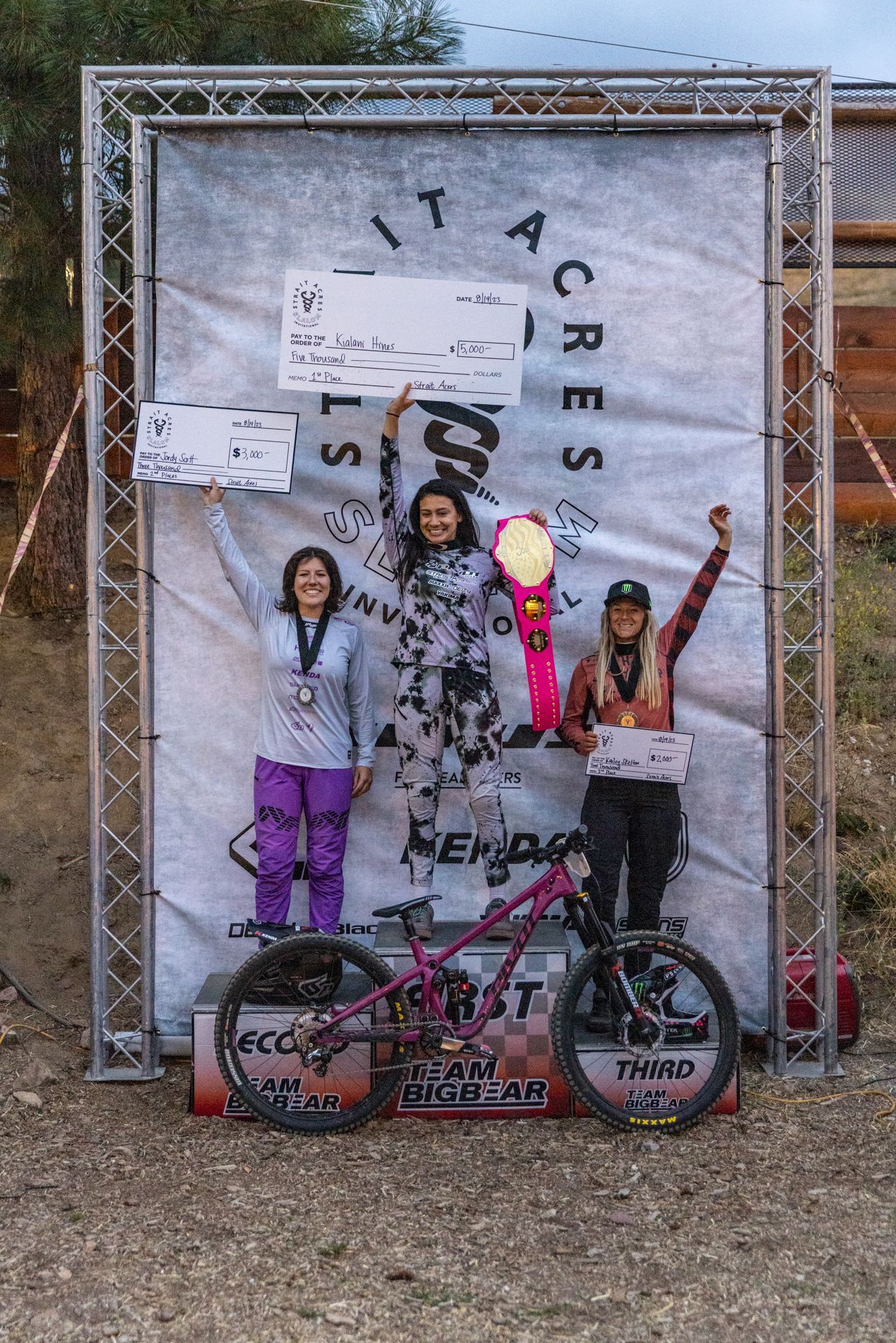 Three mountain bikers stand on a podium after a race, 