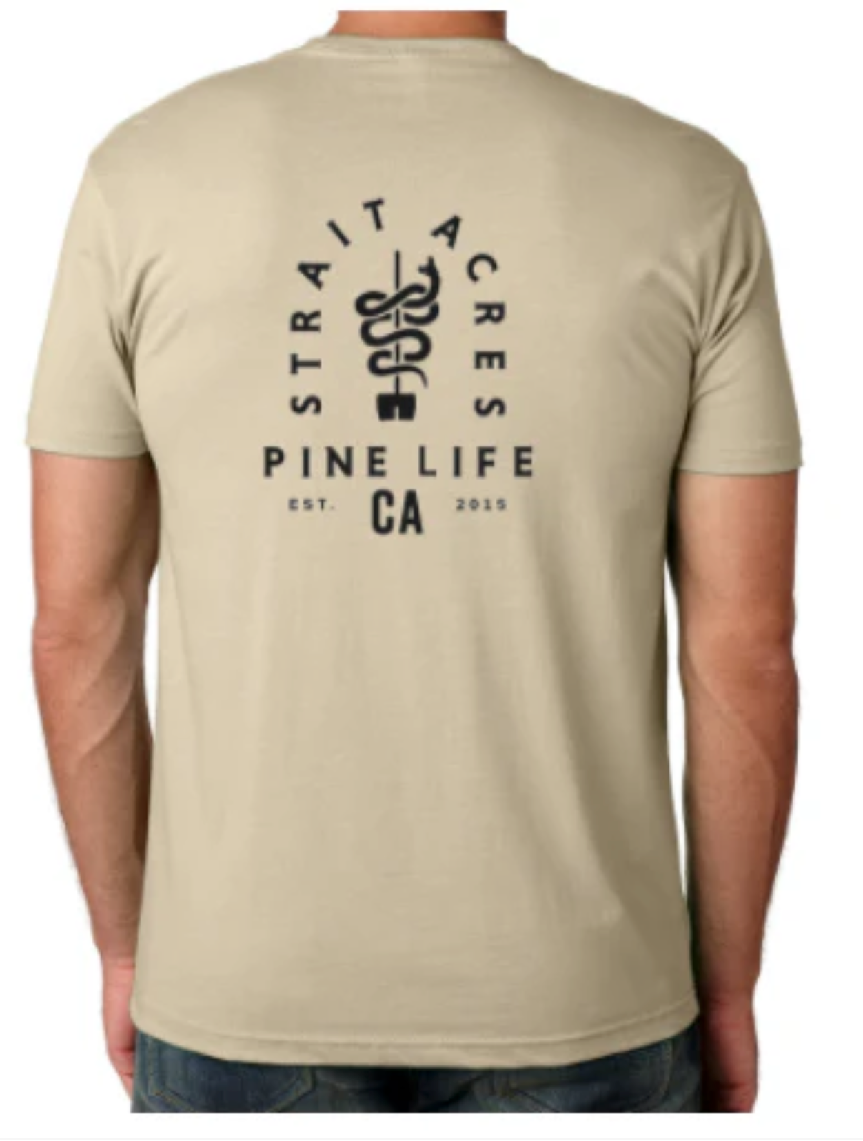 Tan t-shirt with a small black logo on the chest. A person wearing the shirt is standing with one hand in their pocket.