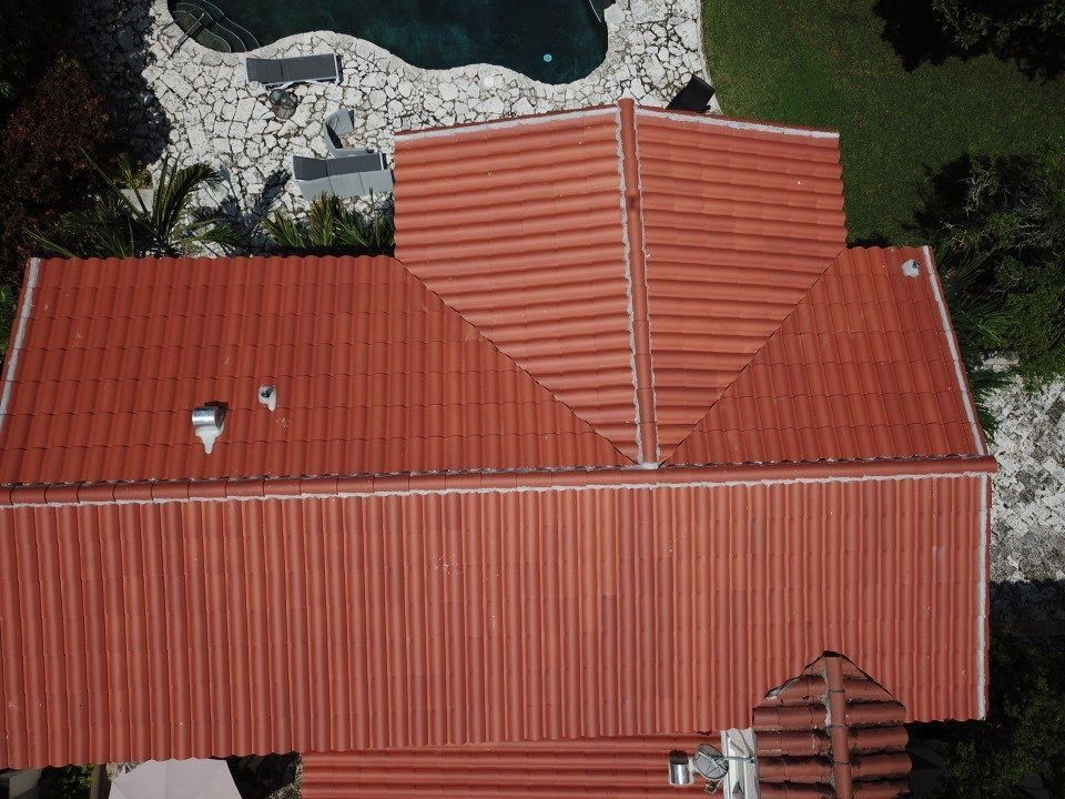 An aerial view of a red tiled roof with a pool in the background