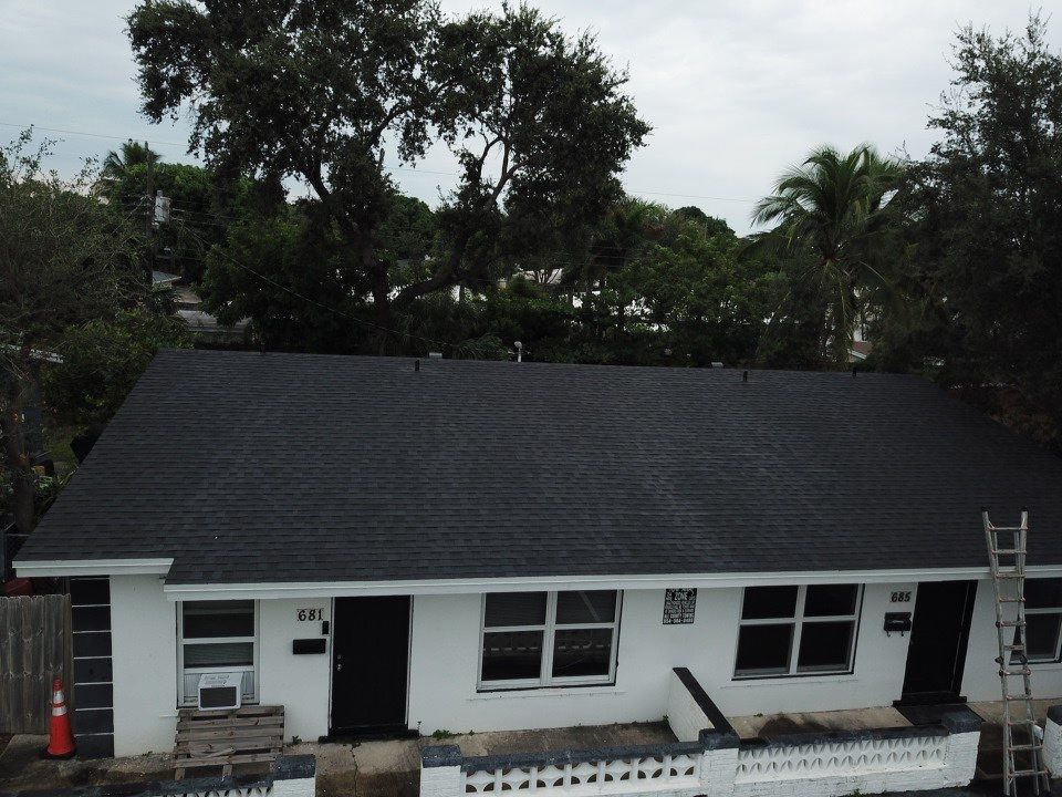 A white house with a black roof and a ladder in front of it
