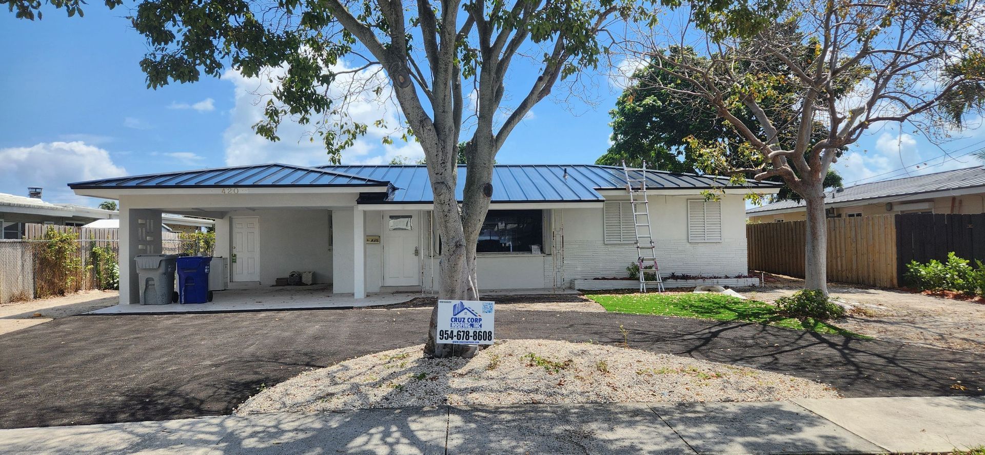 A white house with a blue roof and a tree in front of it.