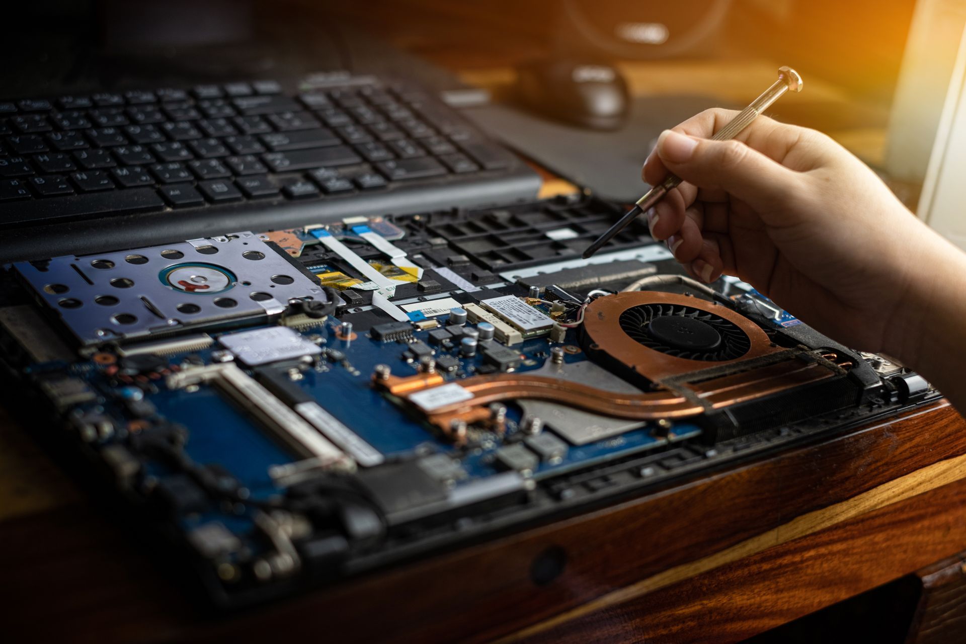 A person is fixing a laptop computer with a screwdriver.