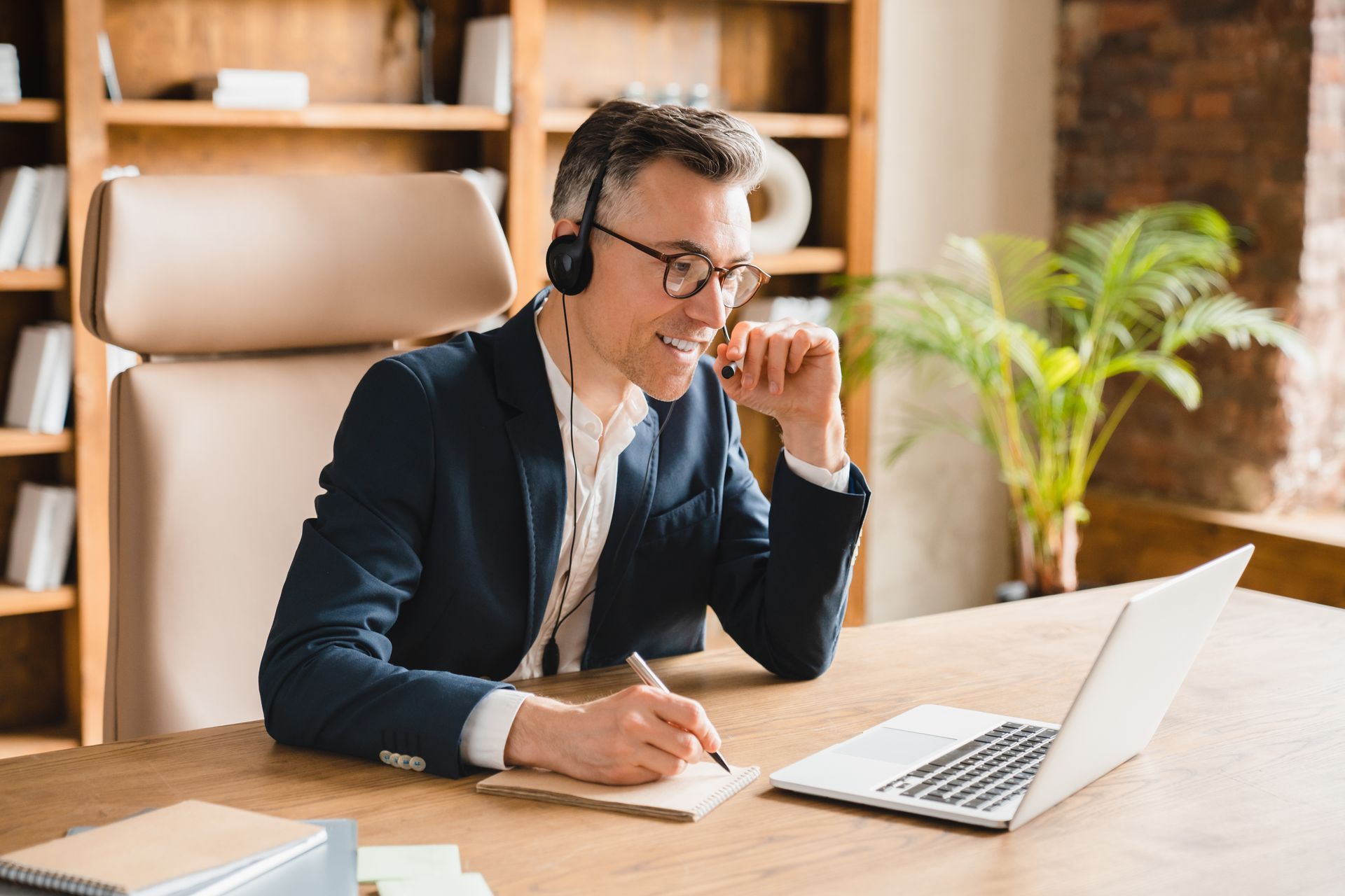 A man wearing headphones is sitting at a desk in front of a laptop computer.
