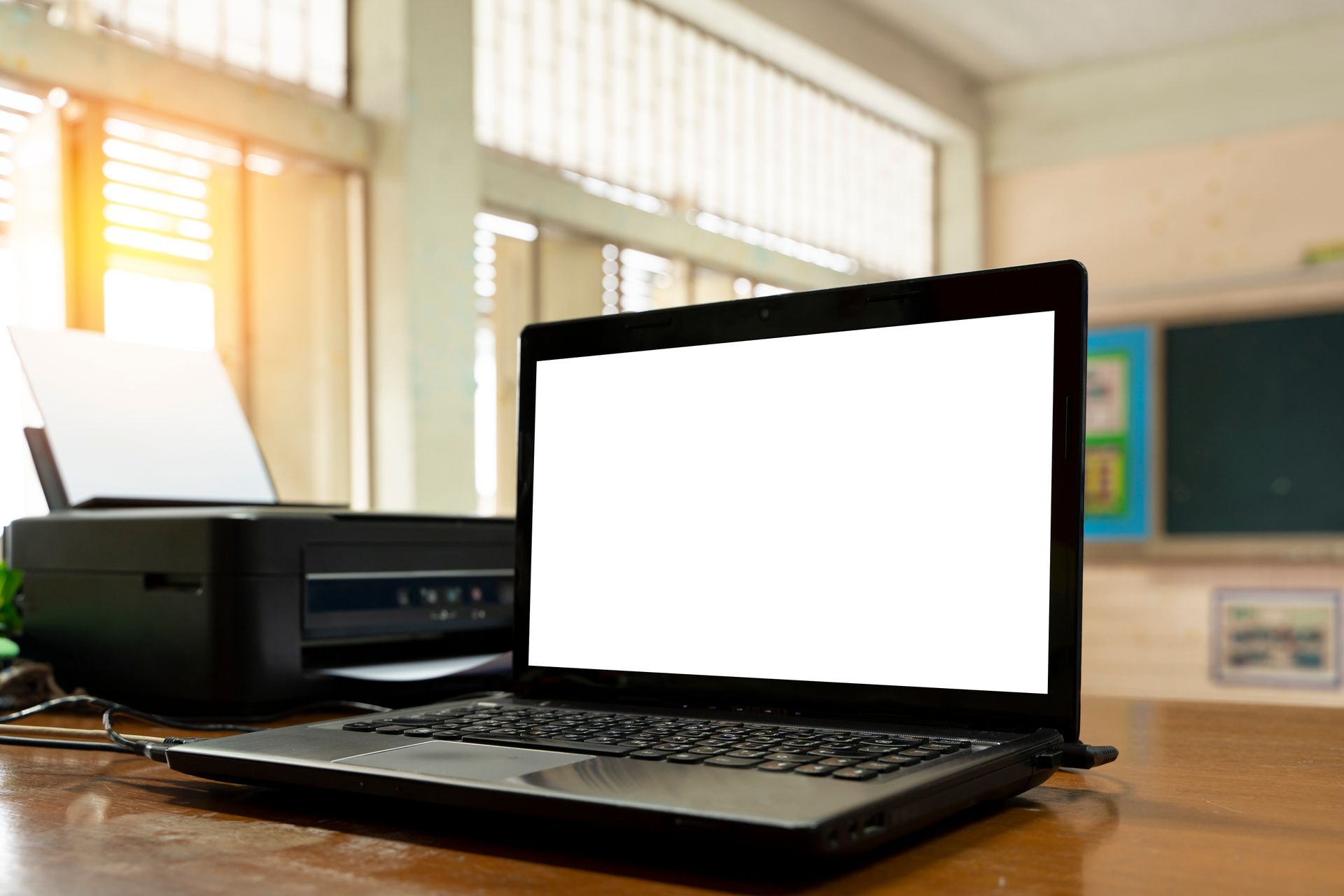A laptop computer is sitting on a wooden desk next to a printer.