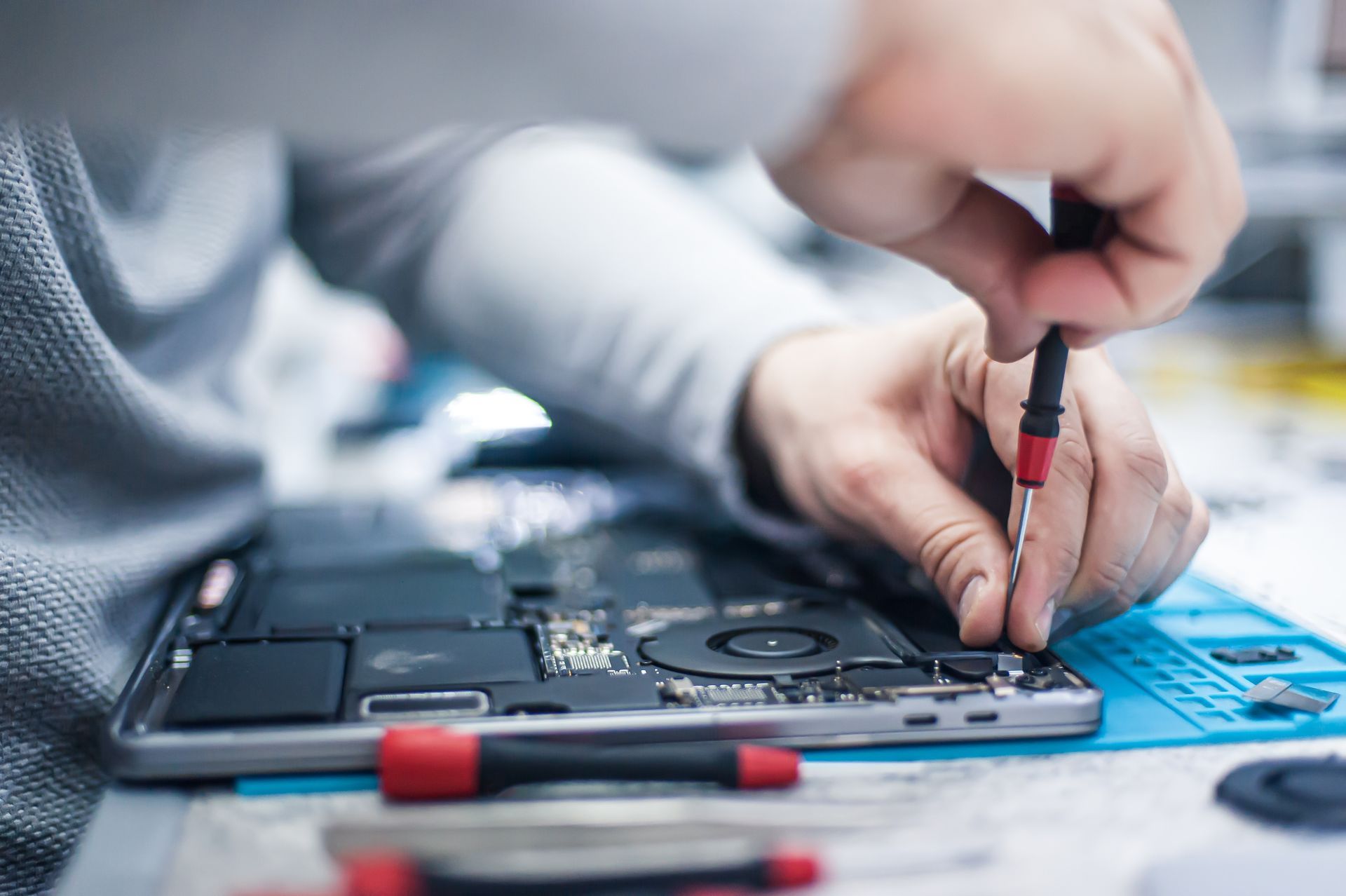 A person is fixing a laptop computer with a screwdriver.