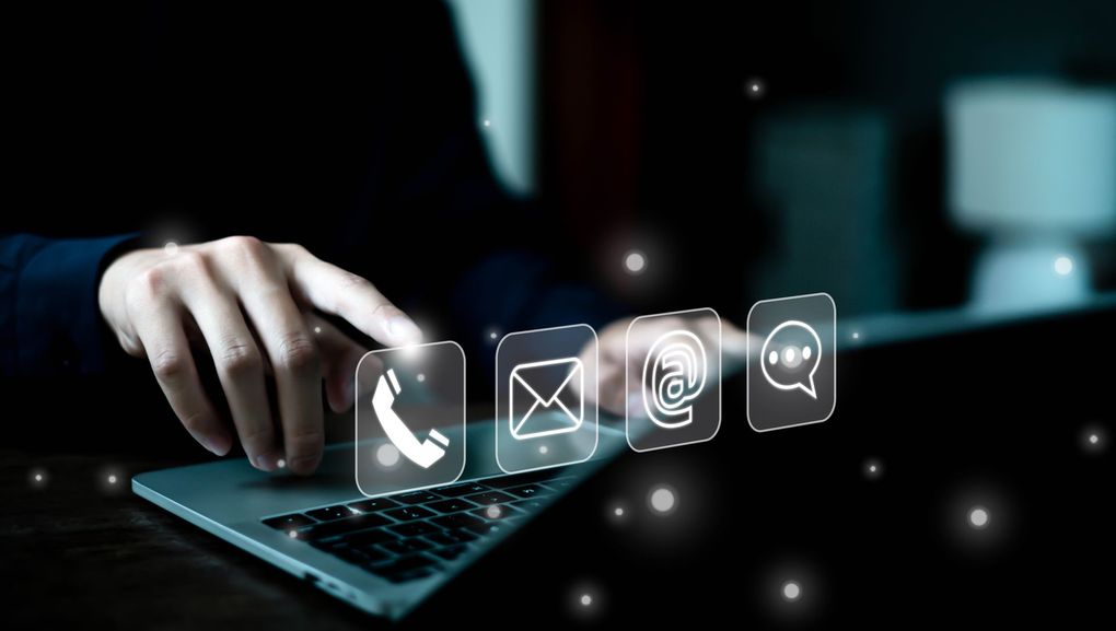 A person is typing on a laptop computer with a contact us icon coming out of it.