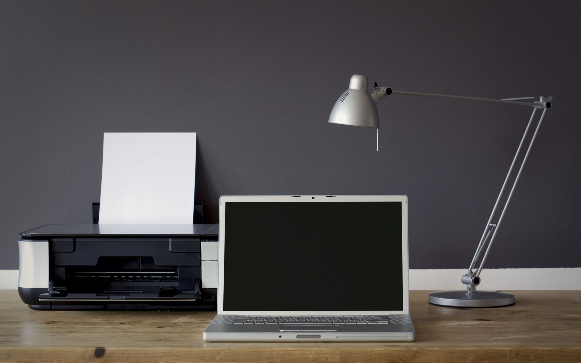 A laptop is sitting on a desk next to a printer and lamp