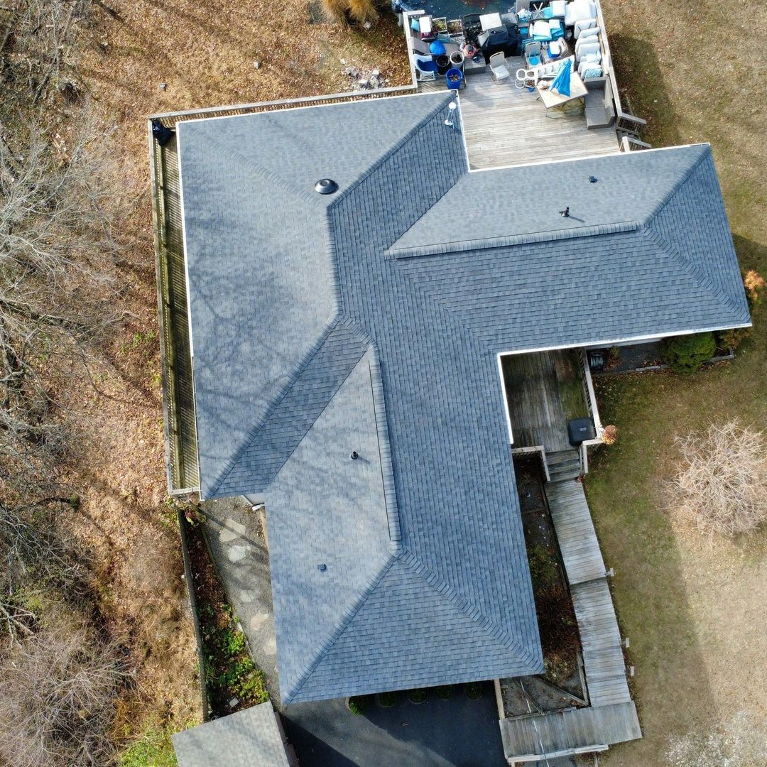 Aerial view of a house under construction with a gray shingle roof and green sheathing.