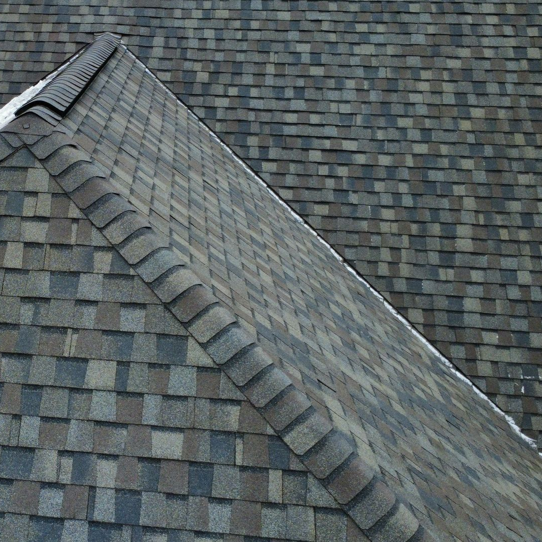 Aerial view of a house under construction with a gray shingle roof and green sheathing.