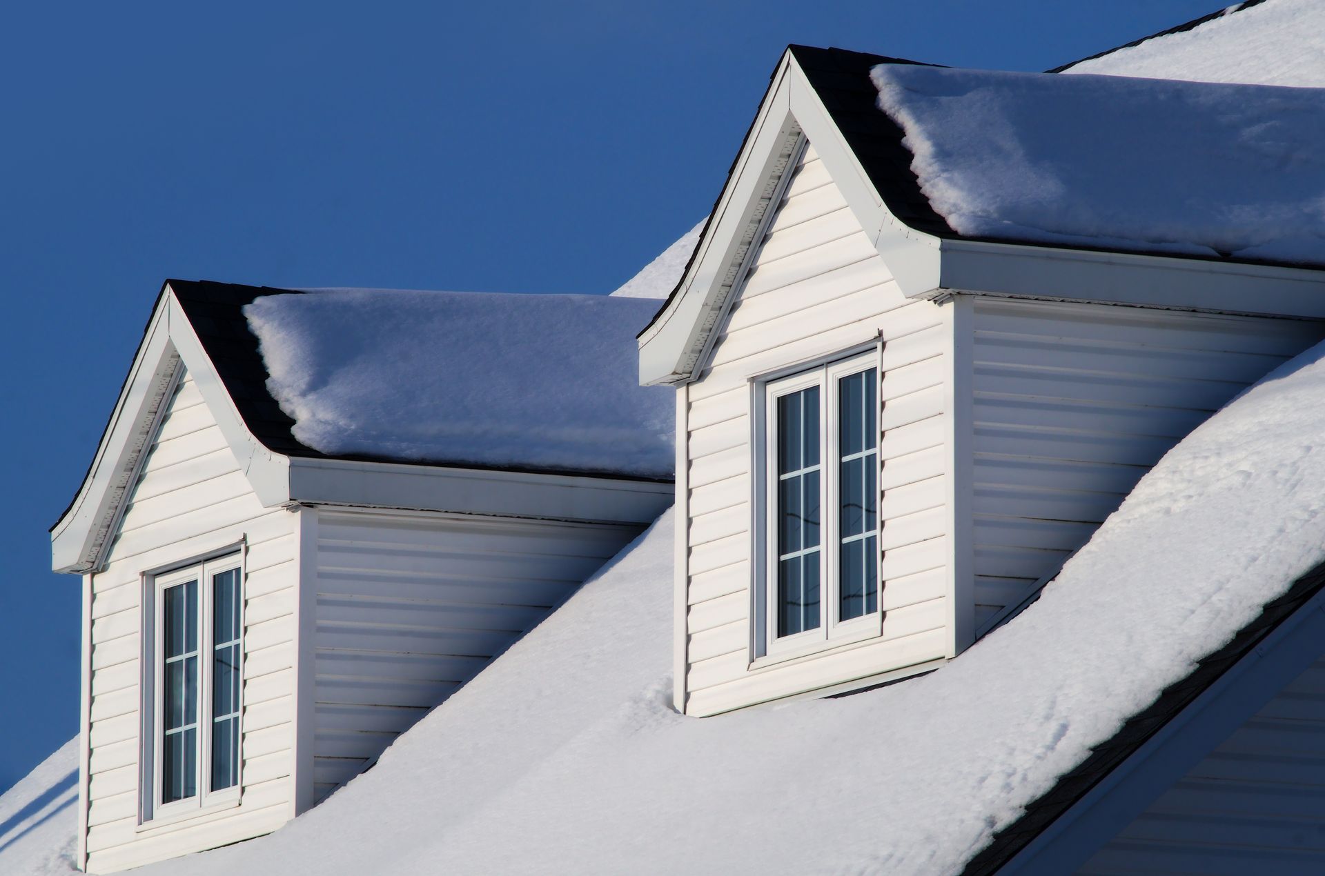 White dormers on a snow-covered roof against a clear blue sky.