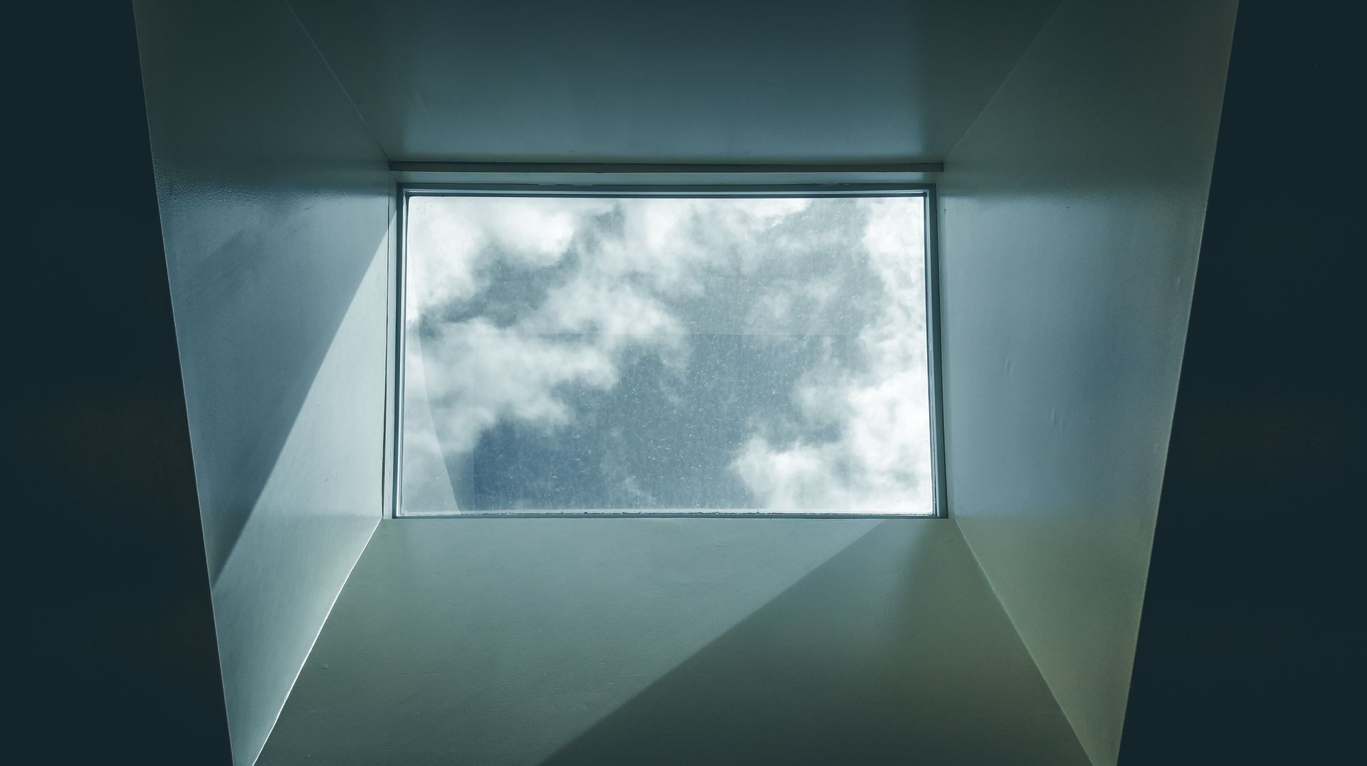 View through a square skylight of cloudy sky framed by gray walls