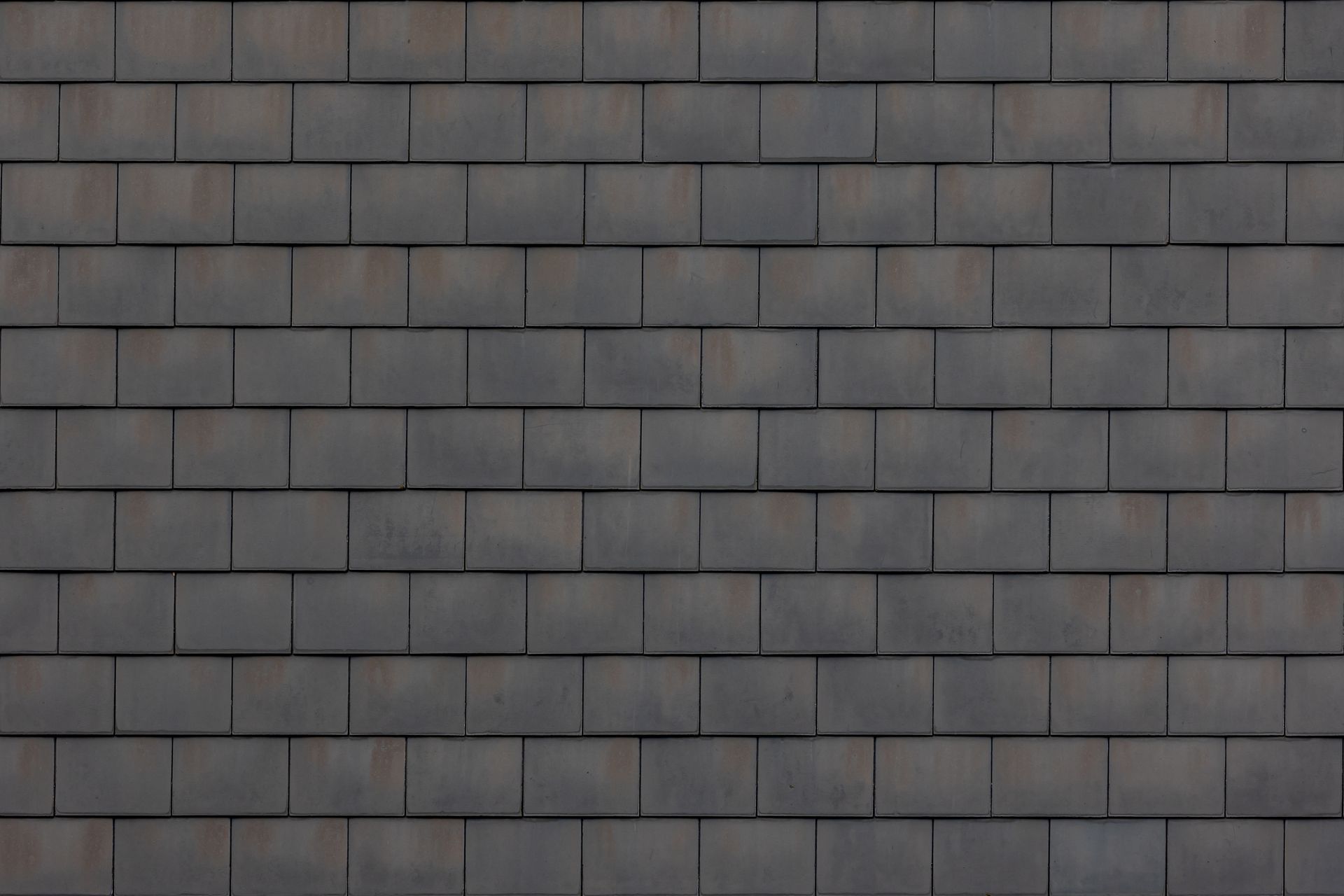 A seamless texture of dark gray rectangular roof shingles arranged in an overlapping, horizontal pattern.