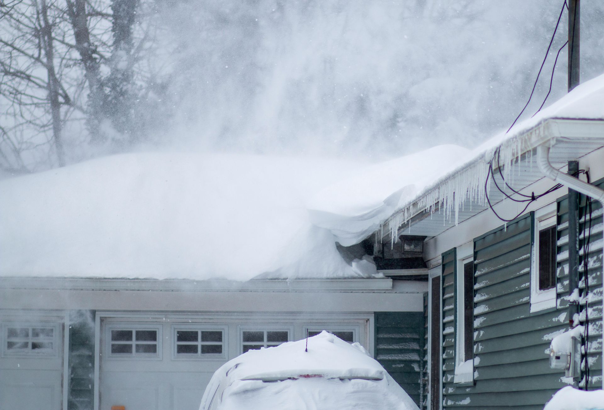 Snow-covered house during a blizzard, with drifts piling up on the roof and blowing snow.