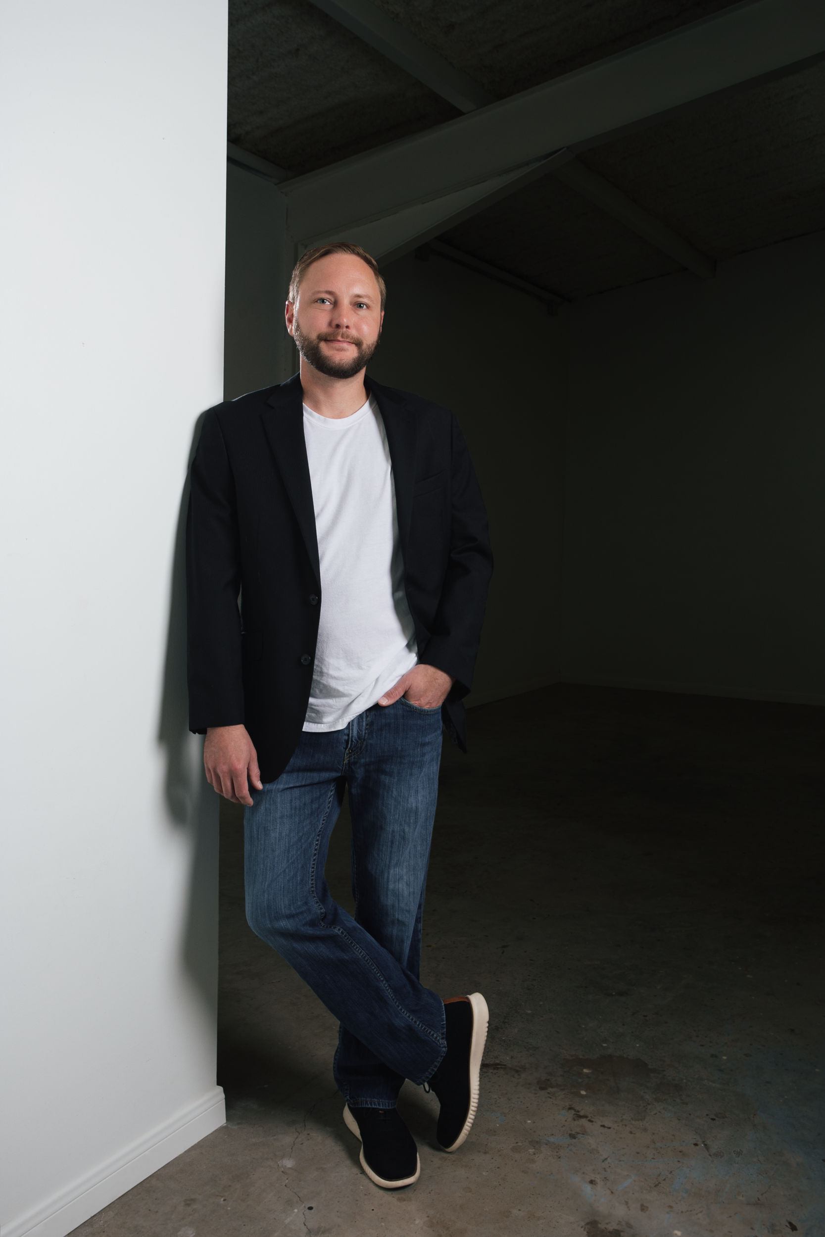 A man is leaning against a wall in an empty room.
