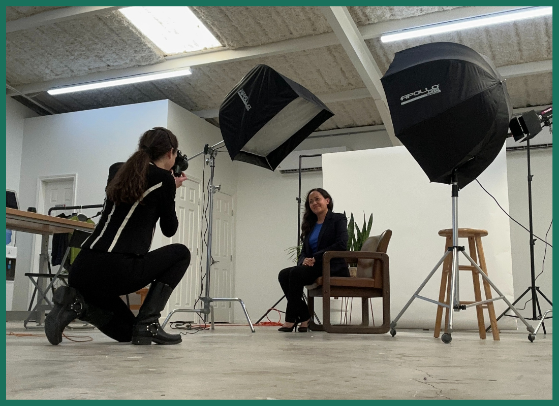 A woman is kneeling down to take a picture of a woman sitting in a chair.