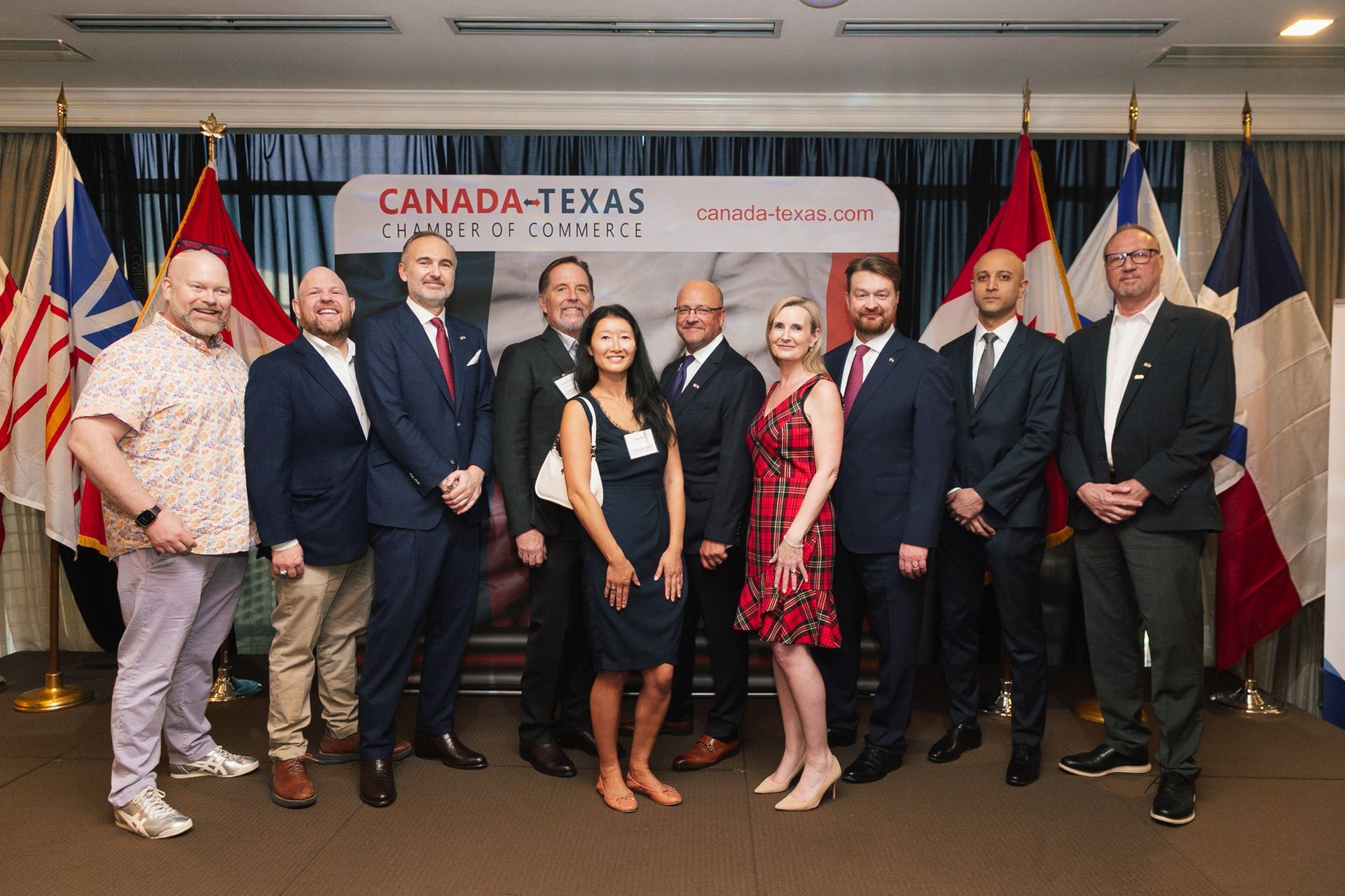 A group of ten business professionals posing for a photo in front of a Canada-Texas Chamber of Commerce backdrop and flags.