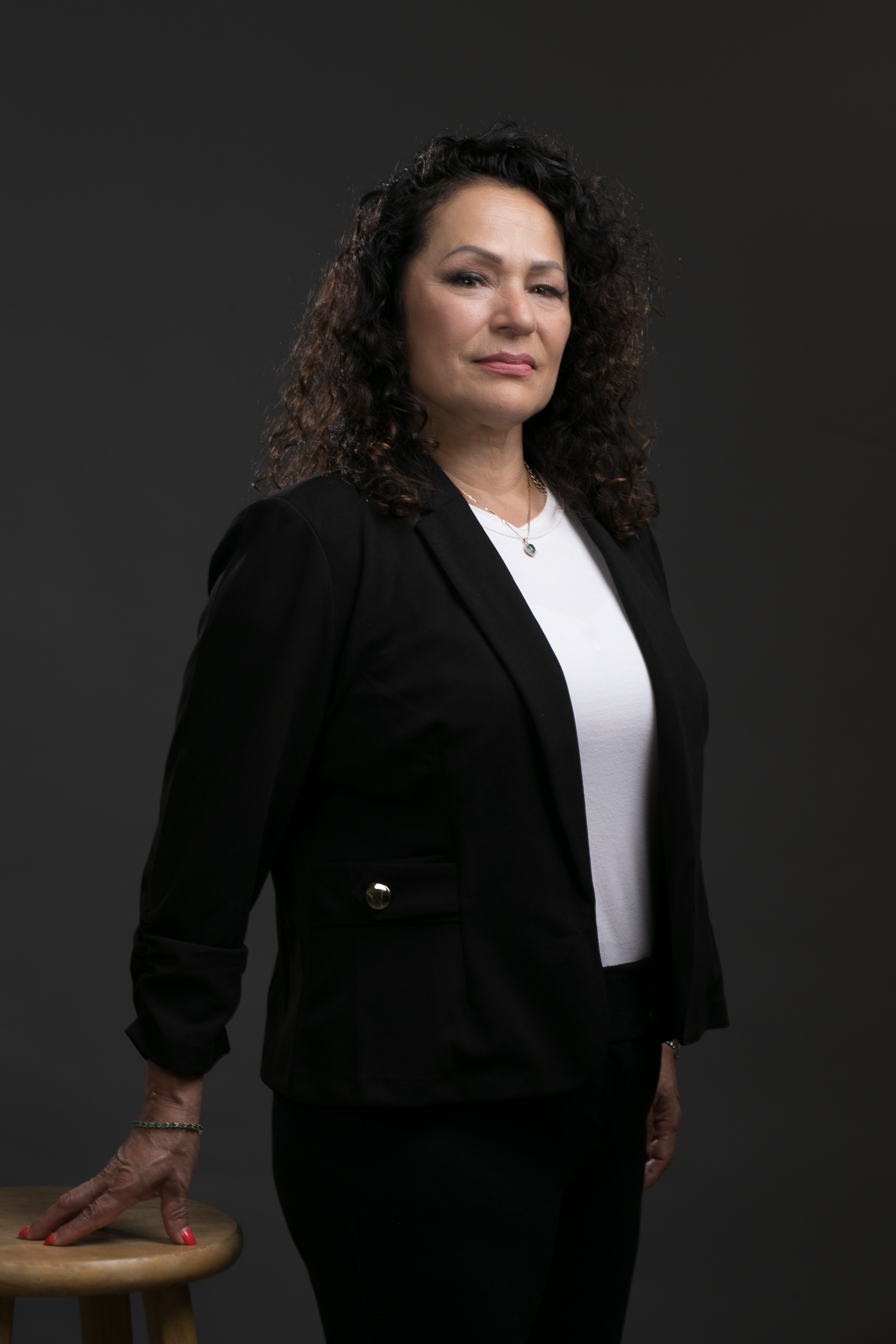 A woman in a black jacket and white shirt is standing next to a stool.
