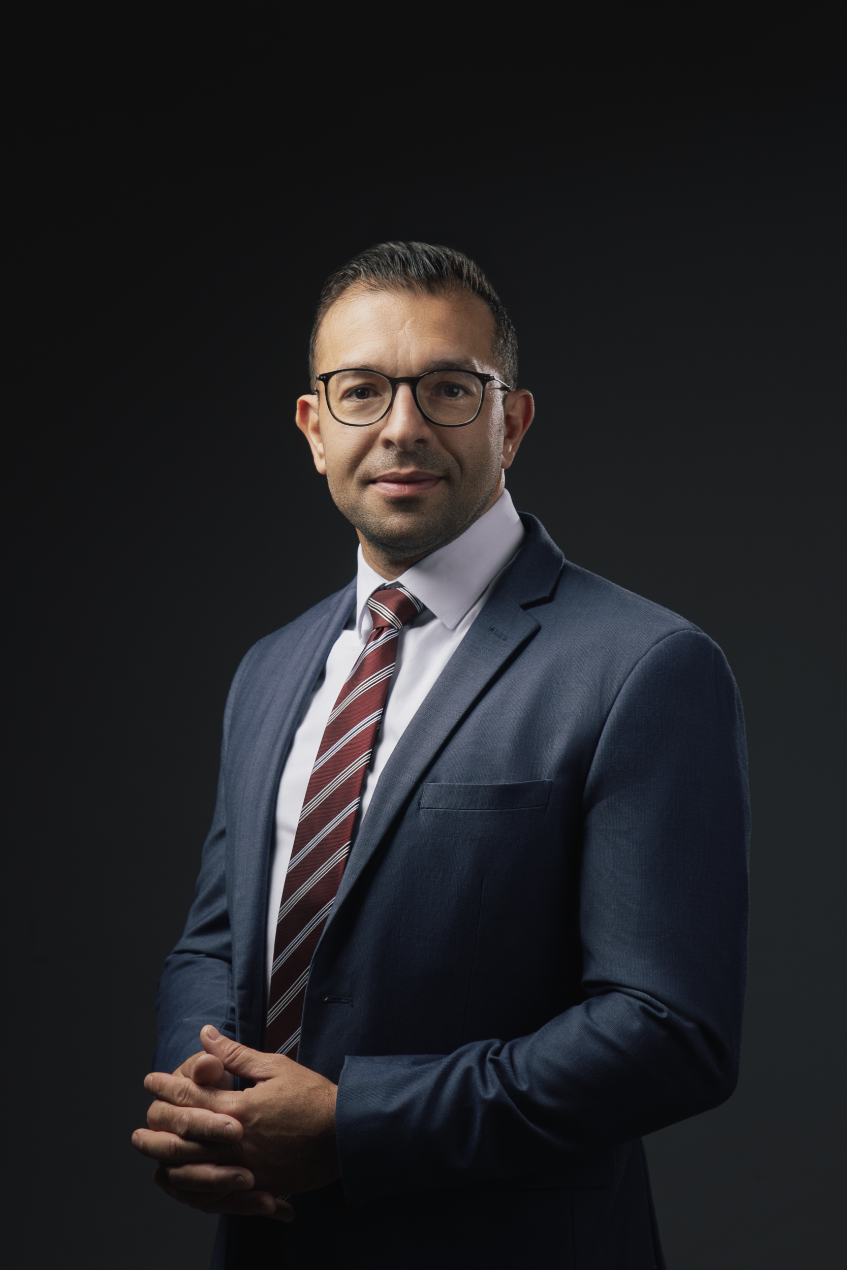 A man in a suit and tie is standing with his hands folded.