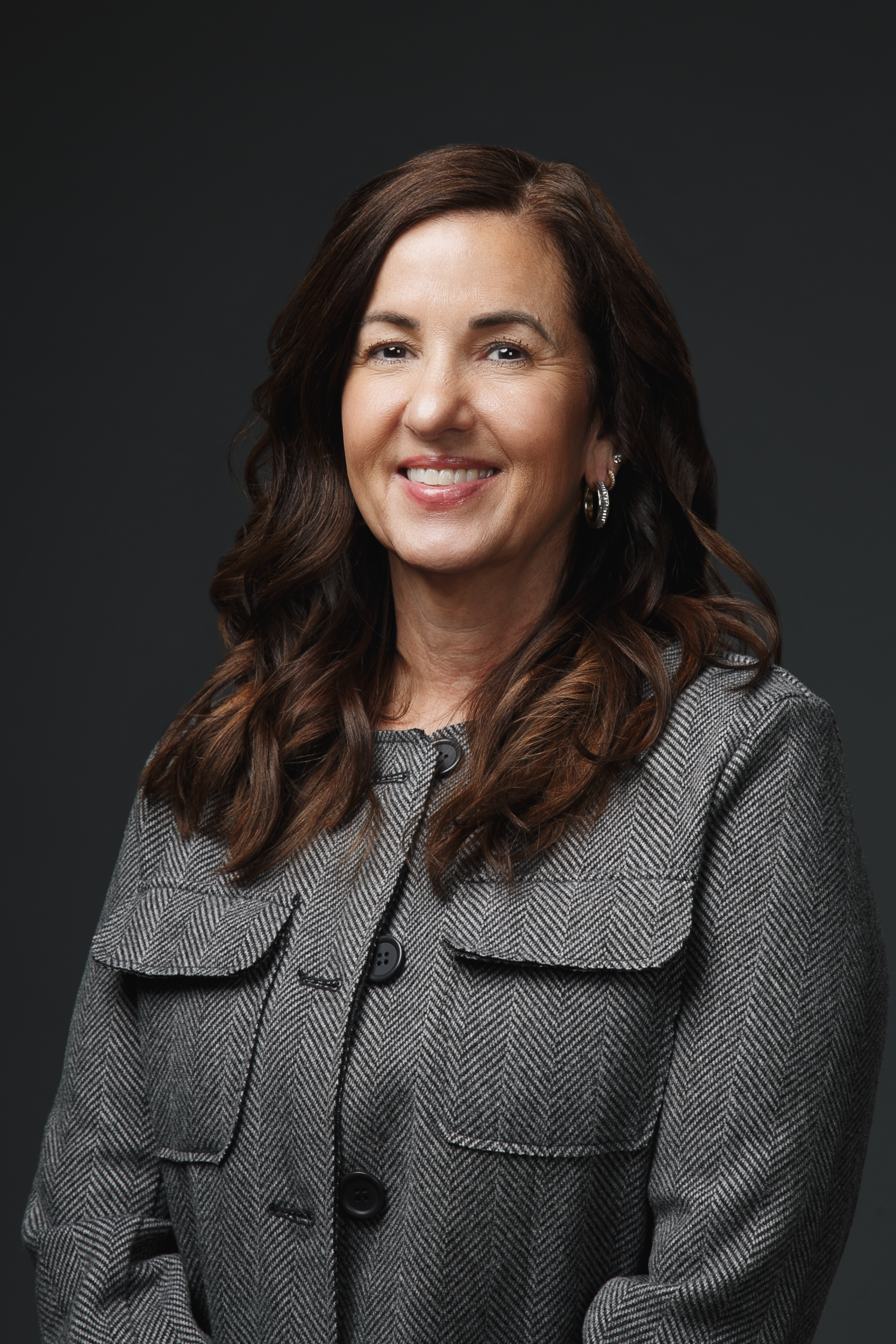 A woman in a gray coat is smiling for the camera.