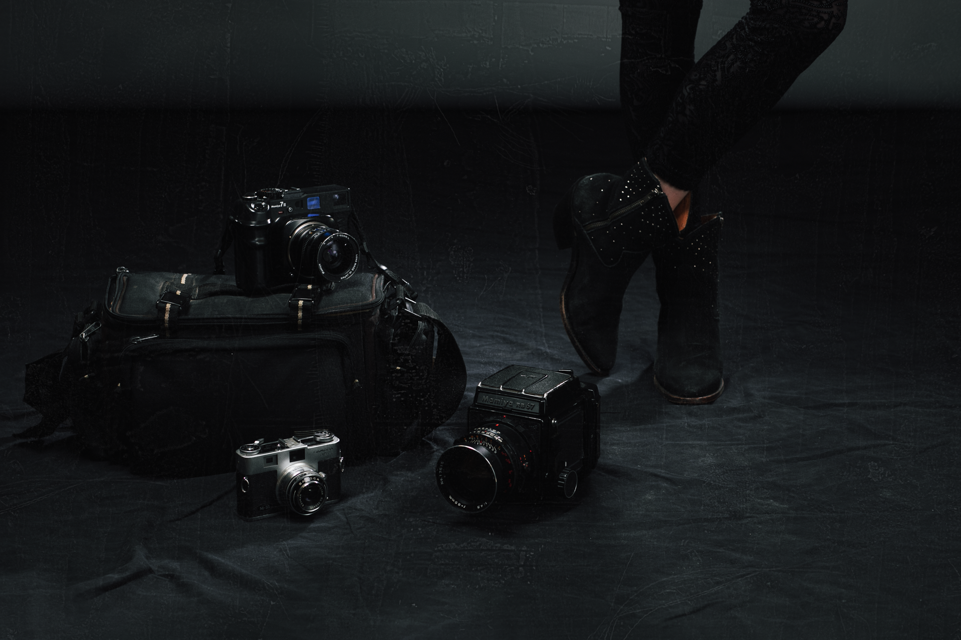 A person is standing next to a pile of cameras and a bag.