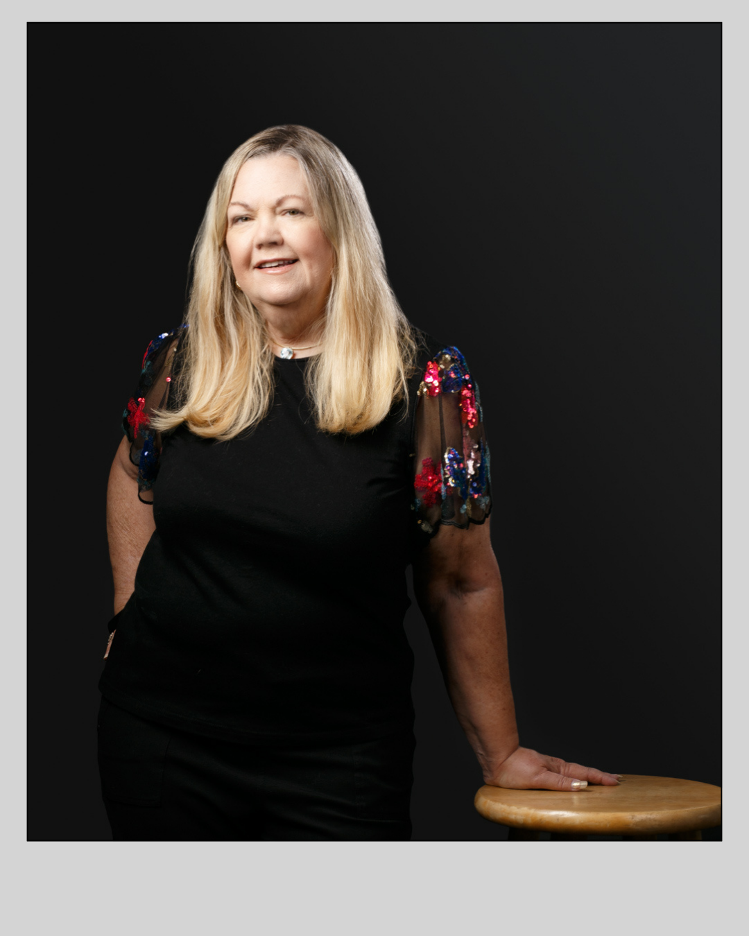 A woman in a black dress is standing next to a wooden stool.