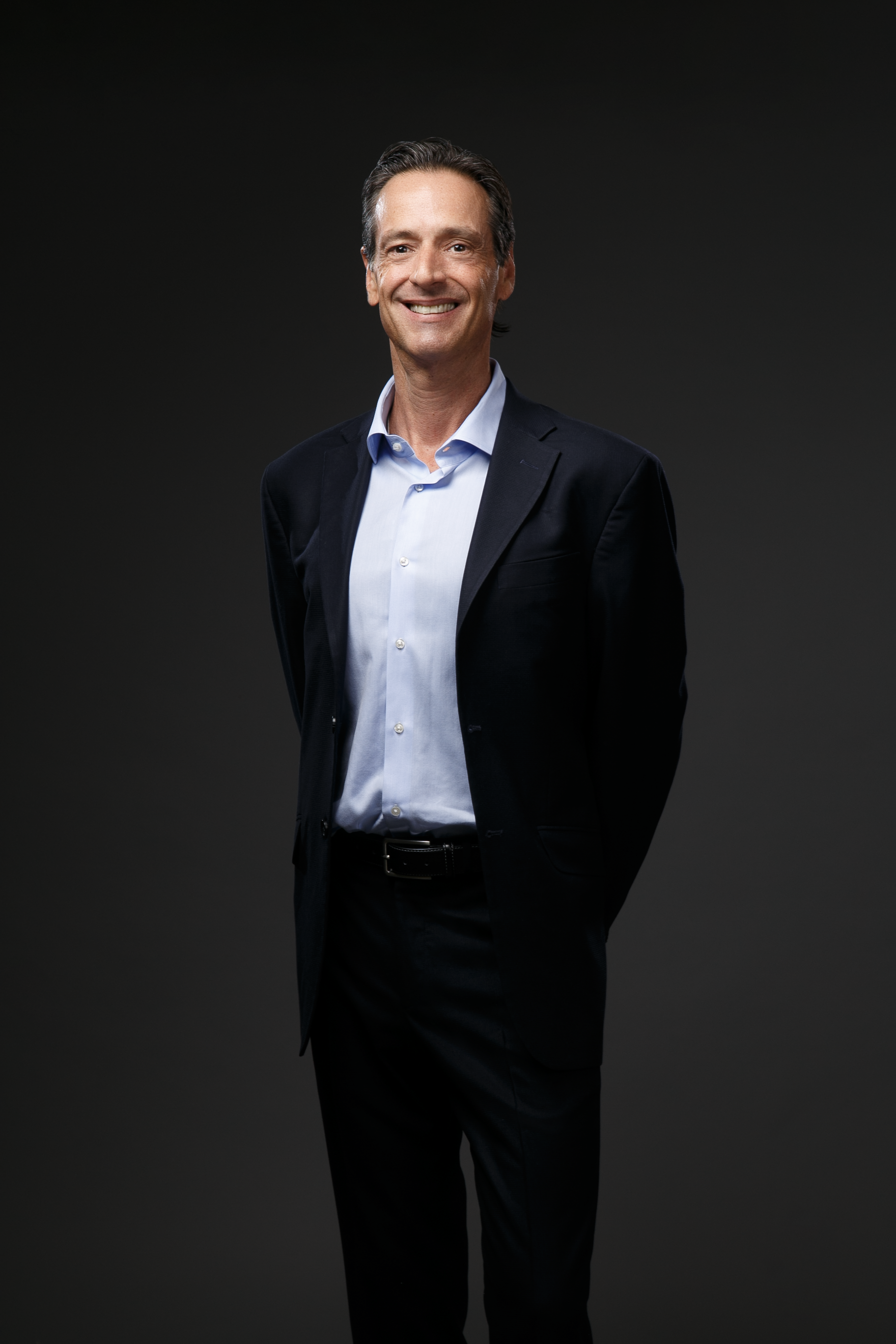 A man in a suit and blue shirt is standing with his hands in his pockets.