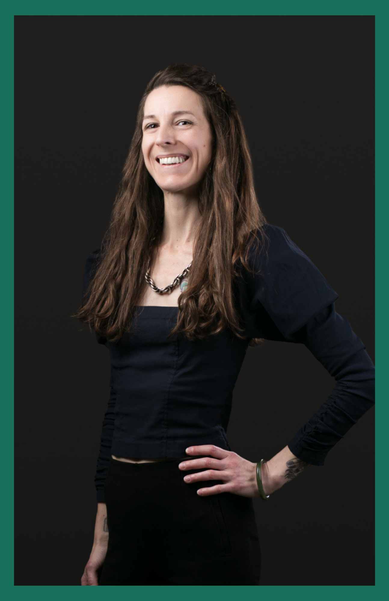 A woman with long hair is smiling and standing with her hands on her hips.