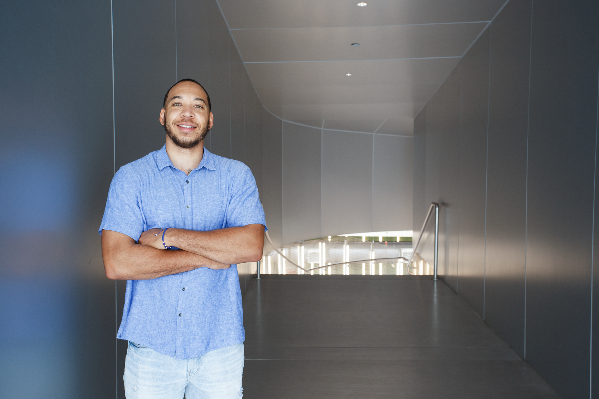 A man in a blue shirt is standing in a hallway with his arms crossed.