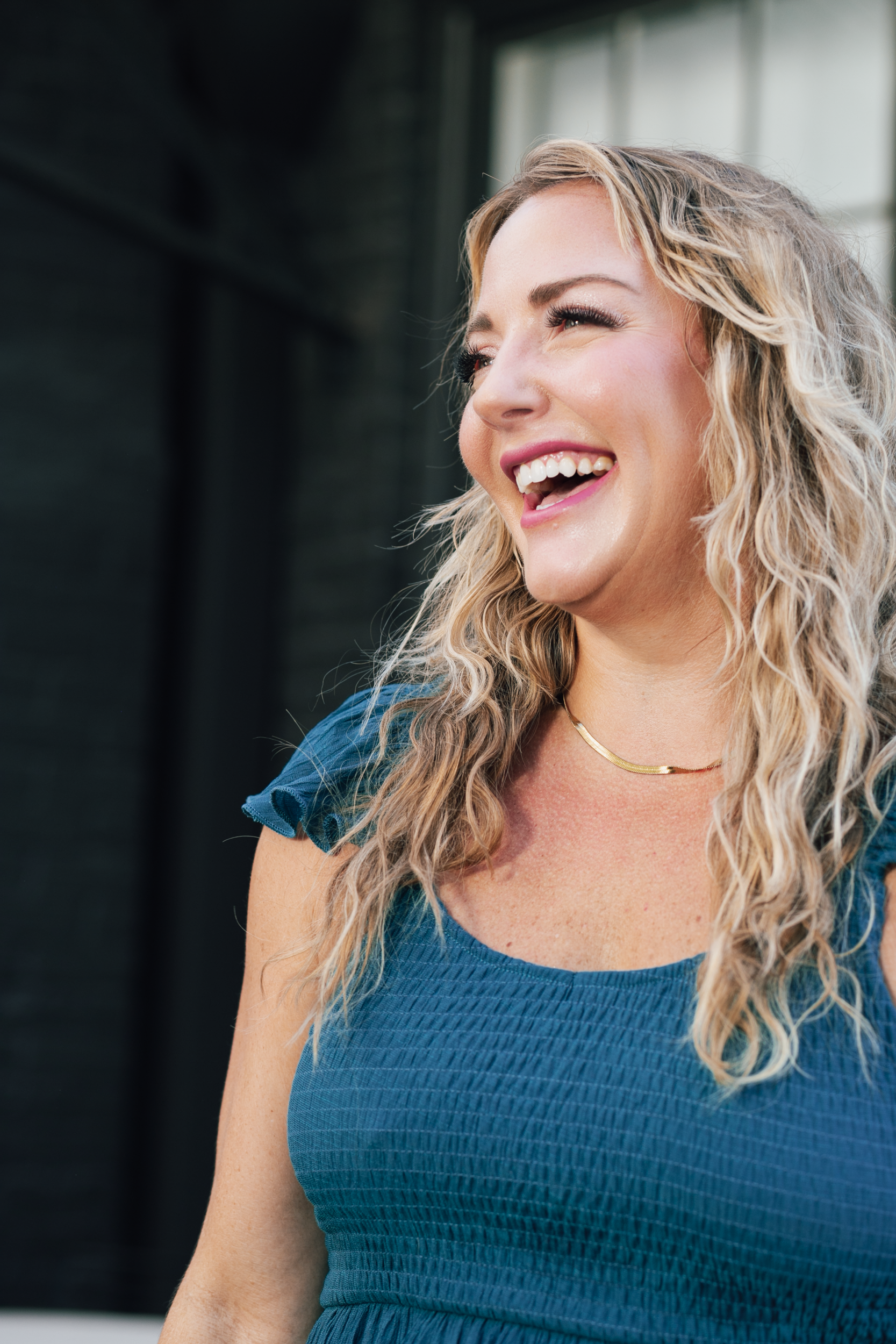 A woman in a blue dress is laughing while standing in front of a building.