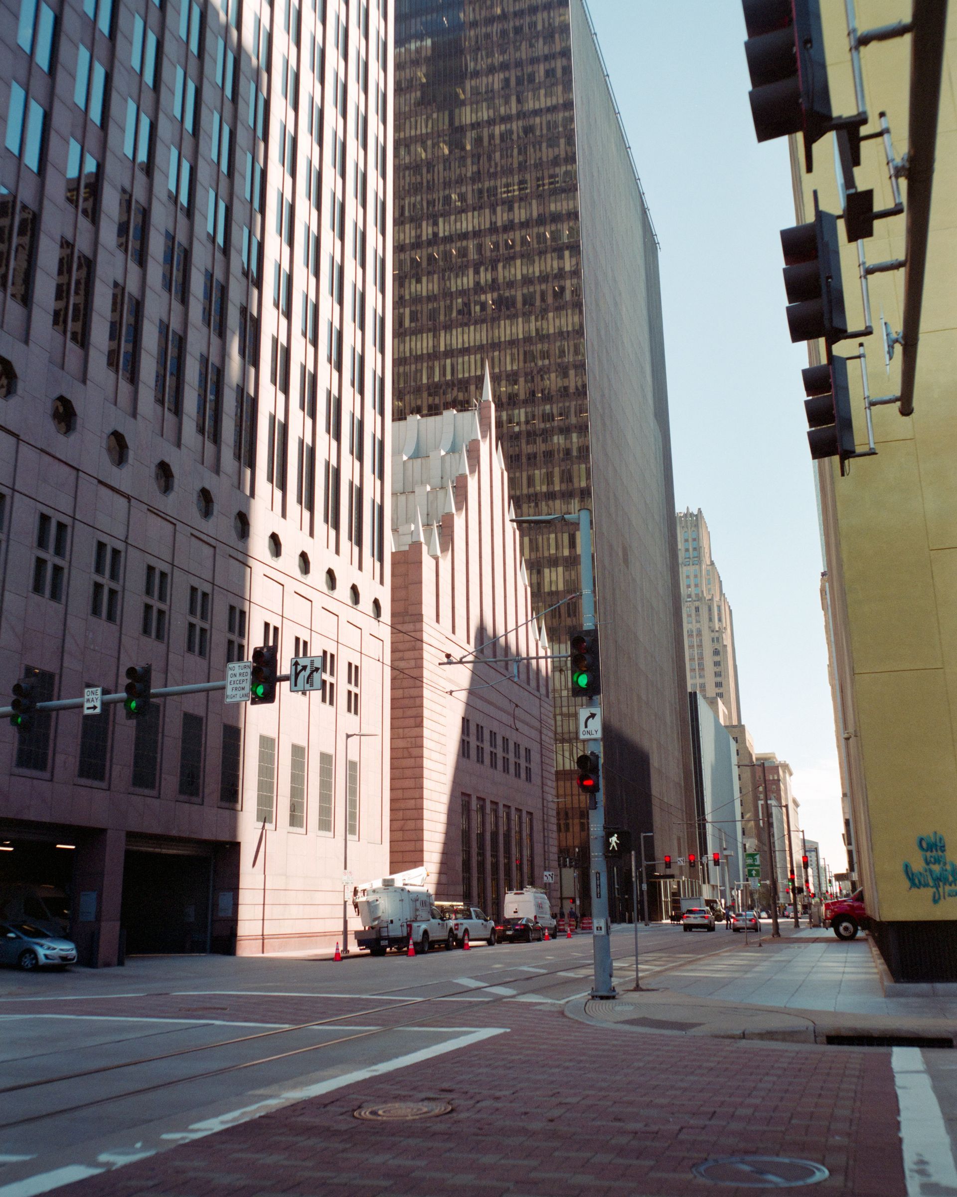 A low-angle view of a city street lined with tall buildings, traffic lights, and a brick intersection.