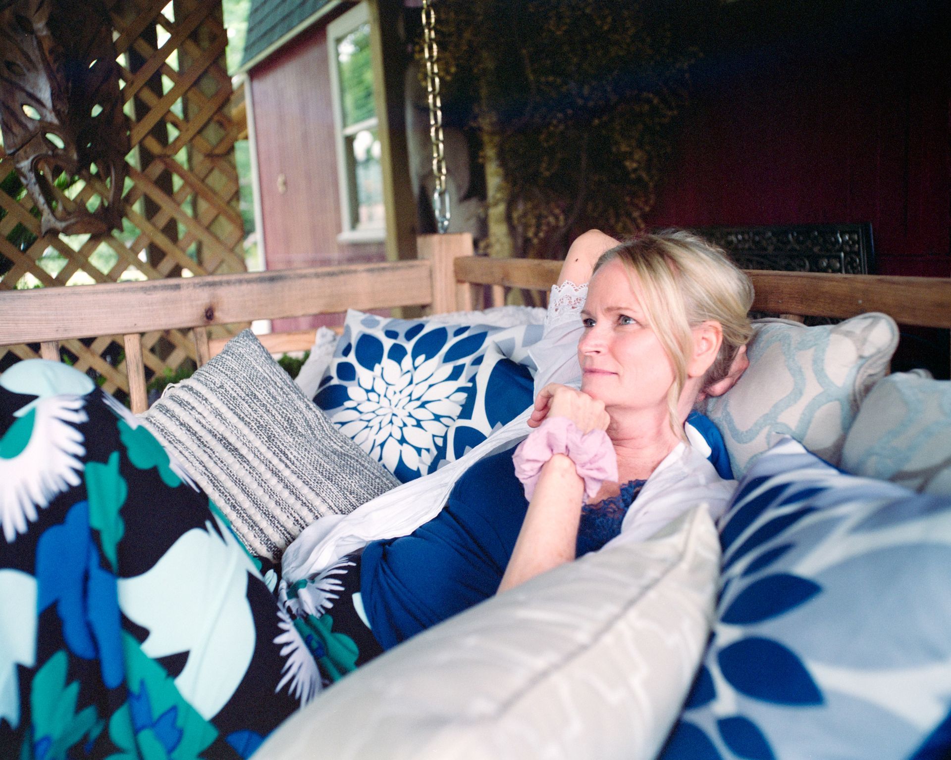 A person lounging on a porch swing with patterned cushions, wearing a dark blue top and white cardigan.