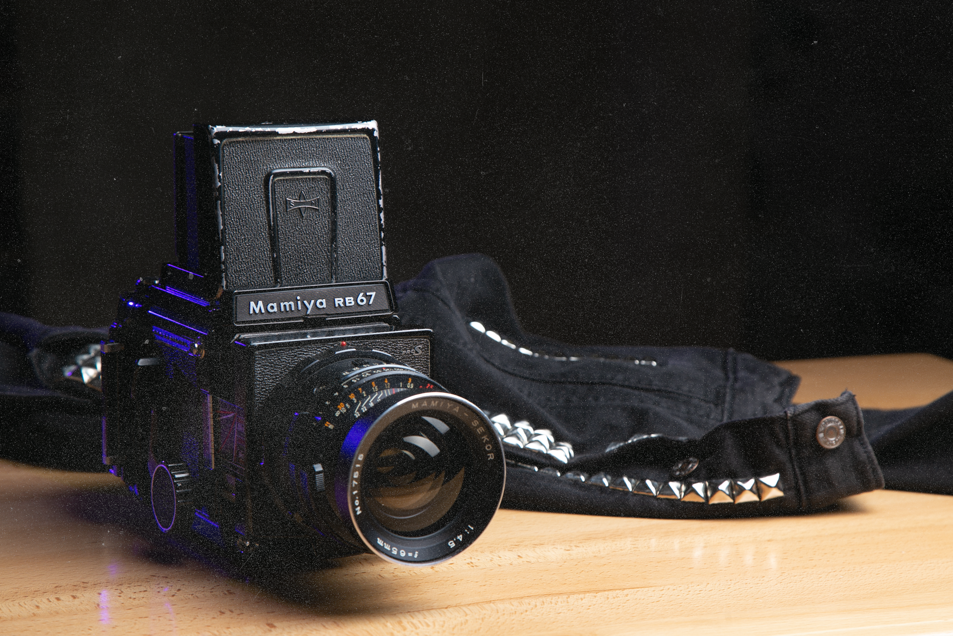 A Mamiya analog camera sits open next to a studded denim jacket.