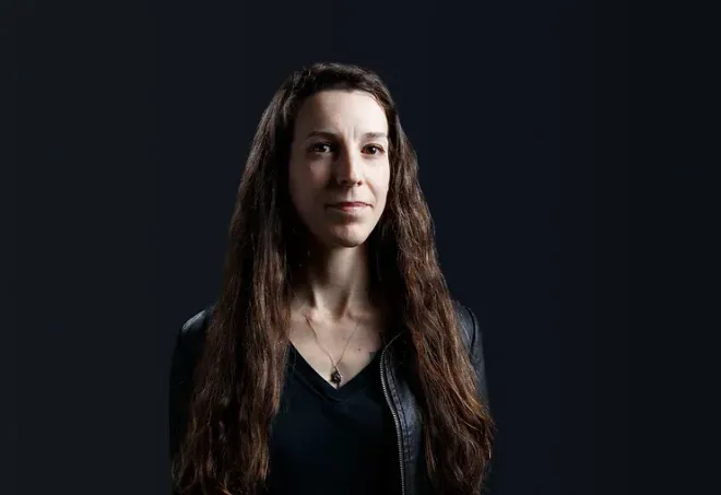 A woman with long hair is standing in front of a black background.