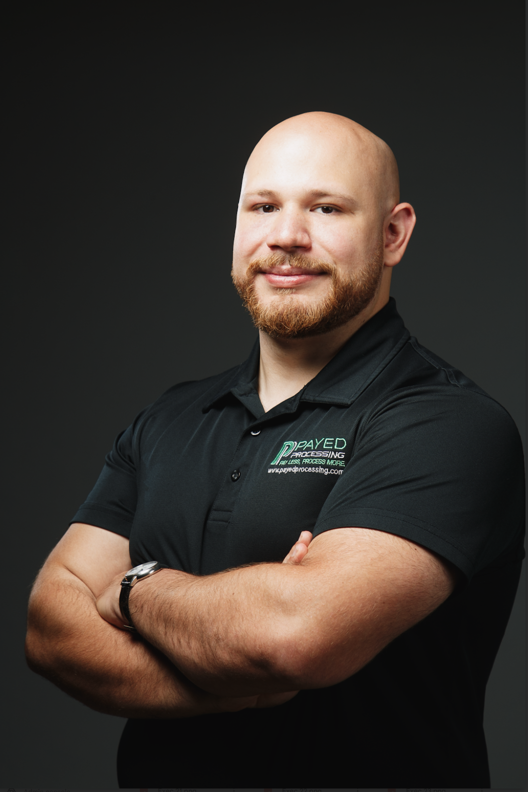 A bald man with a beard is standing with his arms crossed.
