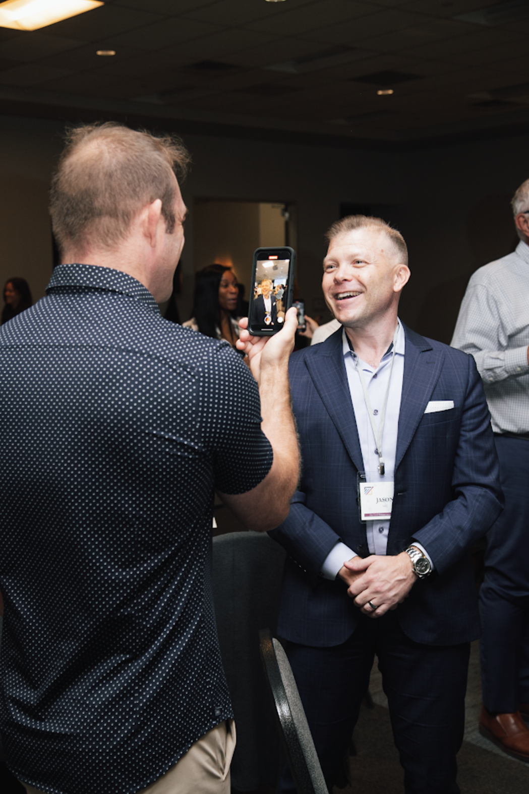 A man in a suit is taking a picture of another man with his cell phone.