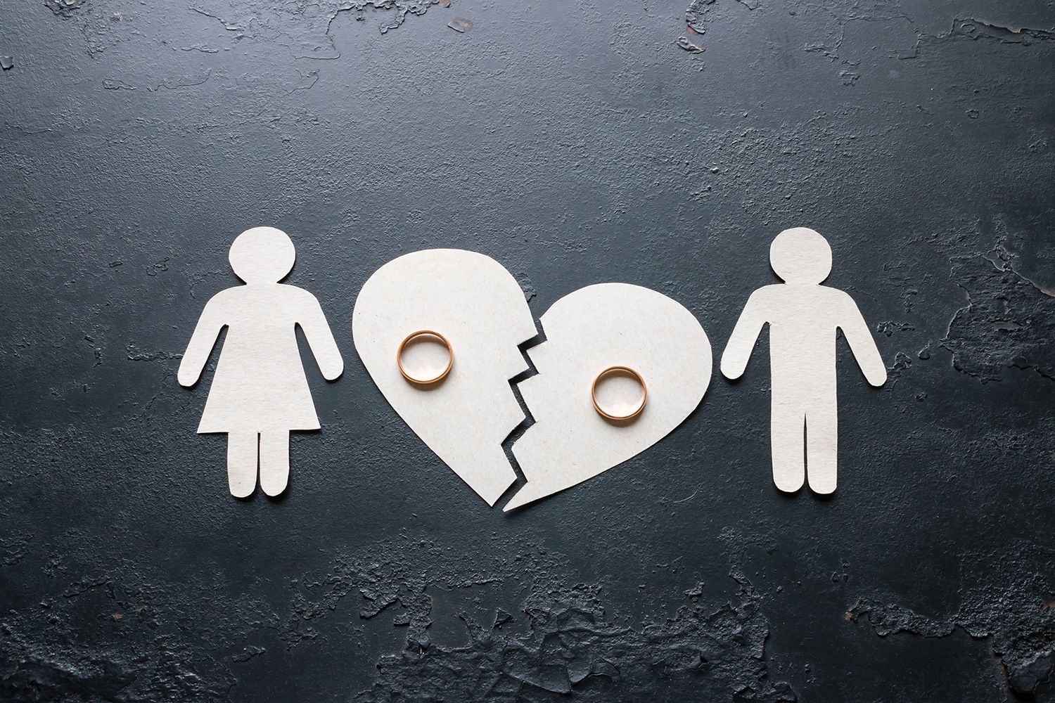 Paper cutouts of a couple beside a broken heart with wedding rings symbolizing divorce.