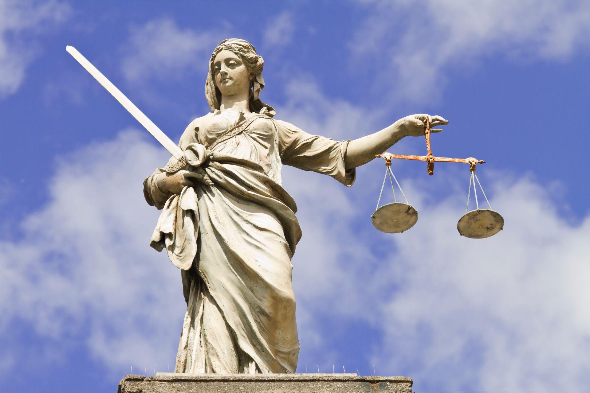 Statue of Lady Justice holding scales and a sword against a cloudy sky.