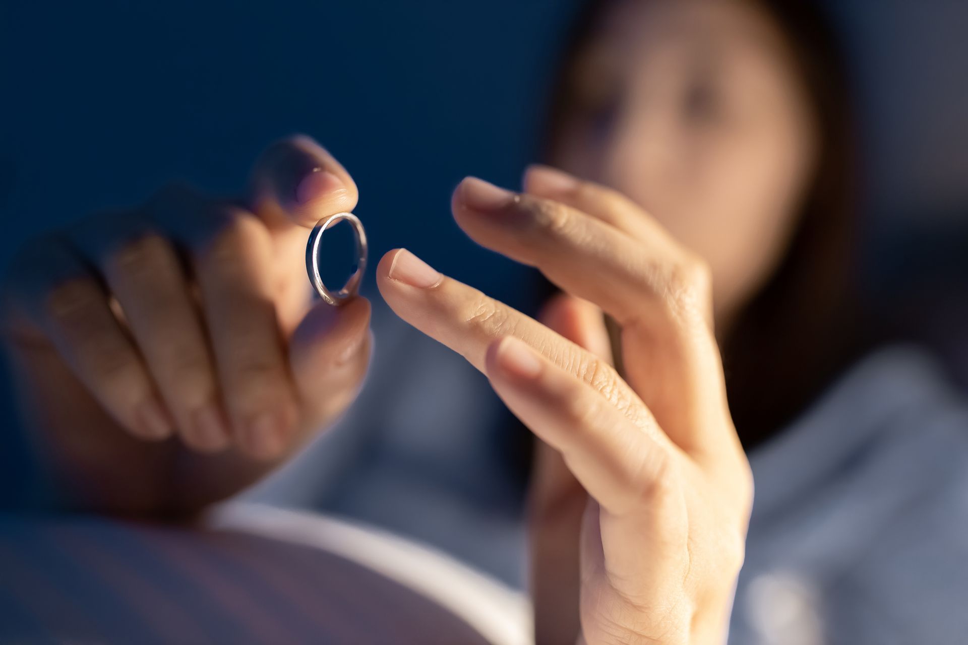 Woman holding a silver ring, lit by soft light, appears to be contemplating. Woman holding a silver ring, lit by soft light, appears to be contemplating.